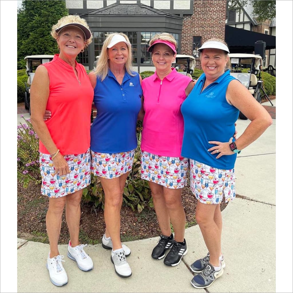 Four women in golf attire posing together outdoors.