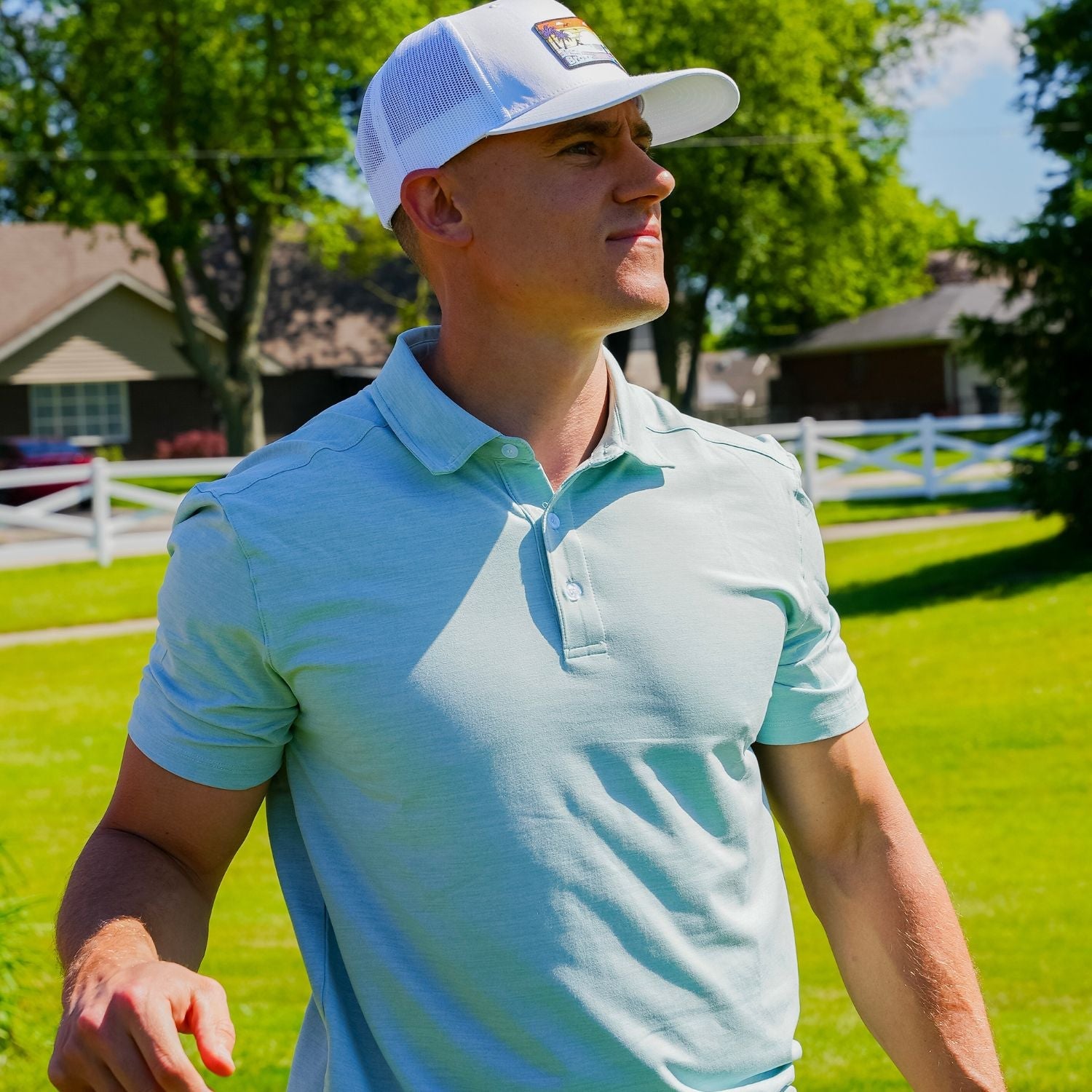 Man wearing a light blue polo shirt and white cap on a golf course