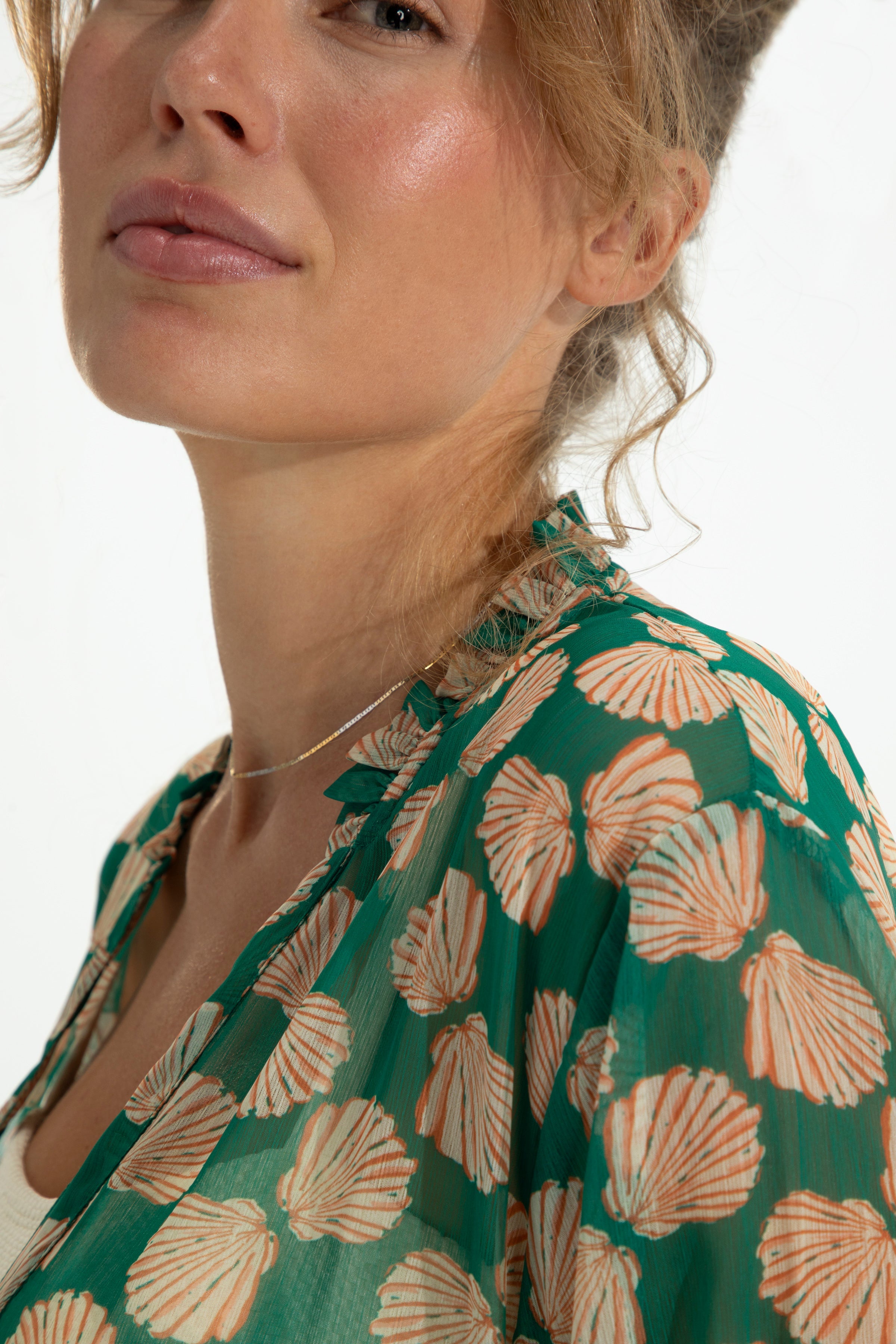 Woman wearing a green blouse with shell pattern on a white background