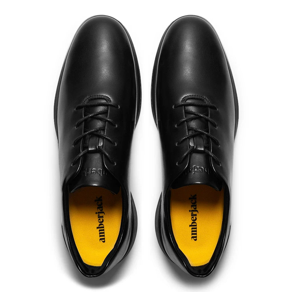 Black leather shoes with yellow soles on a white background