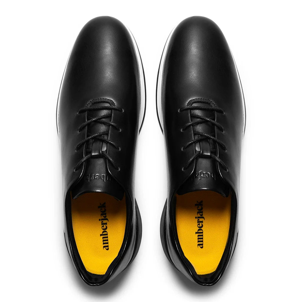 Black leather shoes with yellow soles on a white background