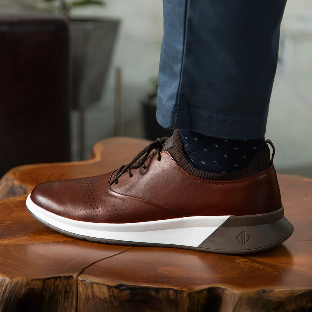 Brown leather shoe with white sole on a wooden surface