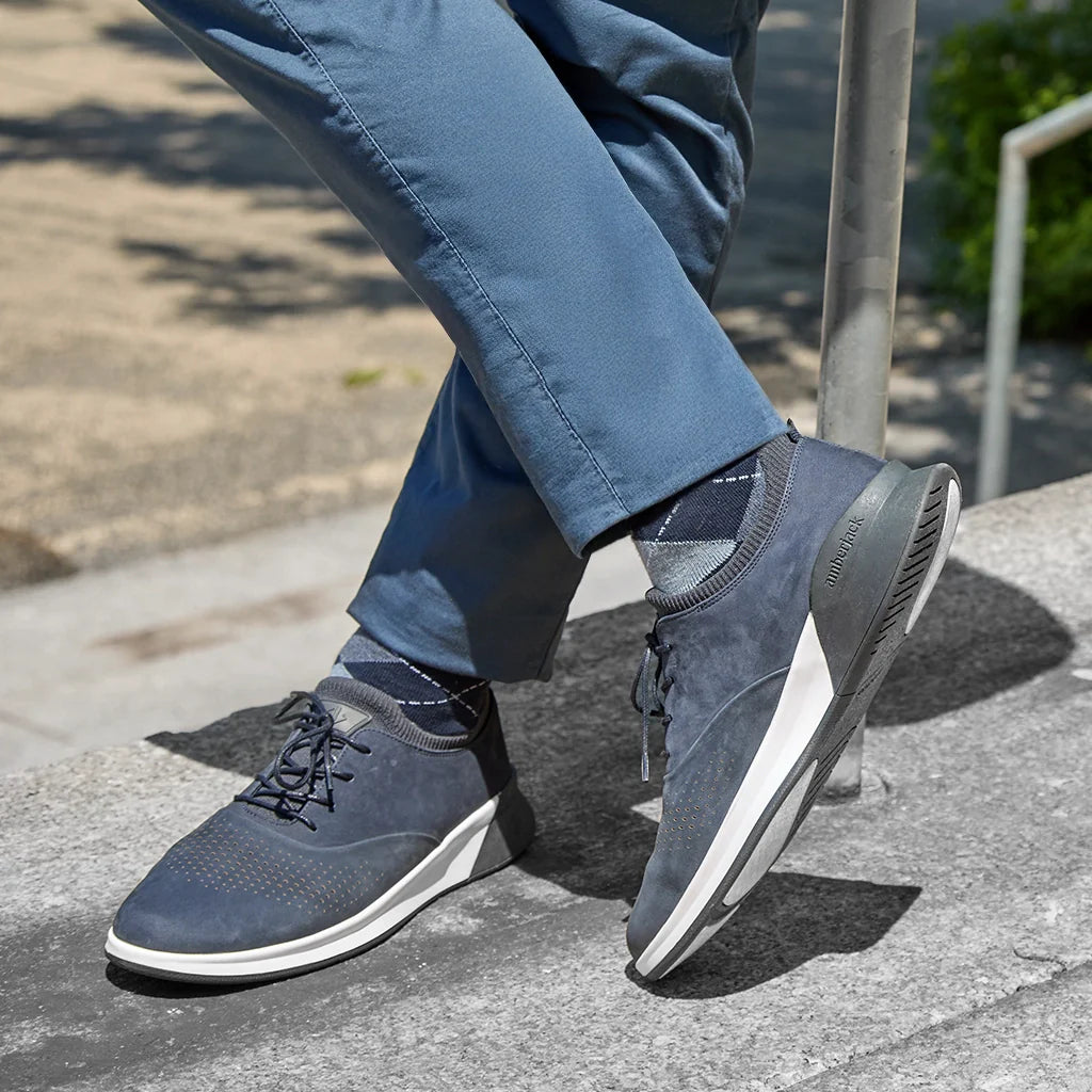 Person wearing blue sneakers with white soles on a sidewalk.