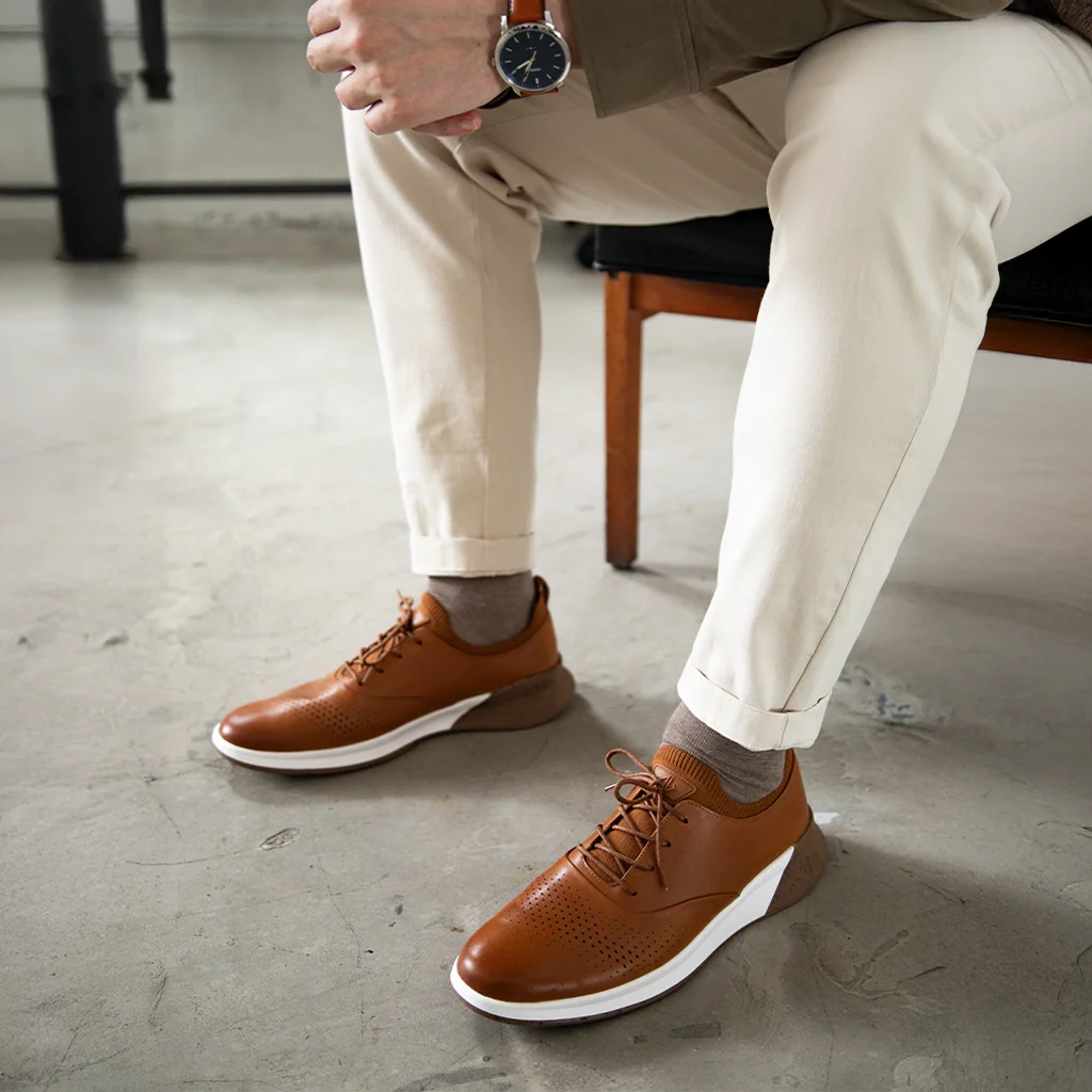 Person wearing brown leather shoes with white soles on a concrete floor.
