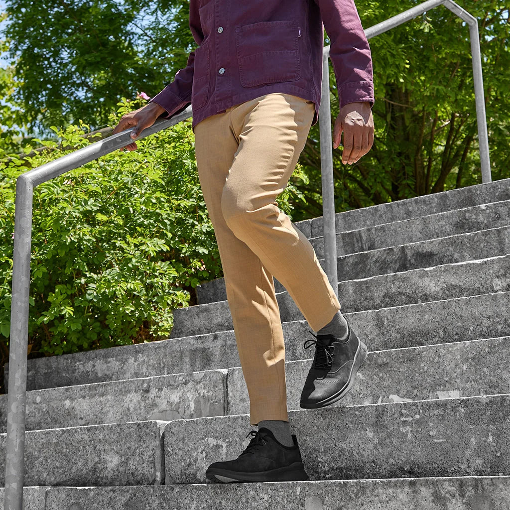 Person in beige pants and black shoes climbing stairs outdoors with greenery in the background