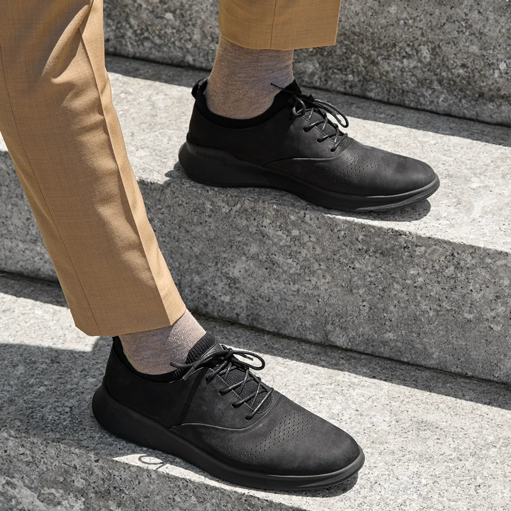 Person wearing black leather shoes and beige pants on a concrete surface