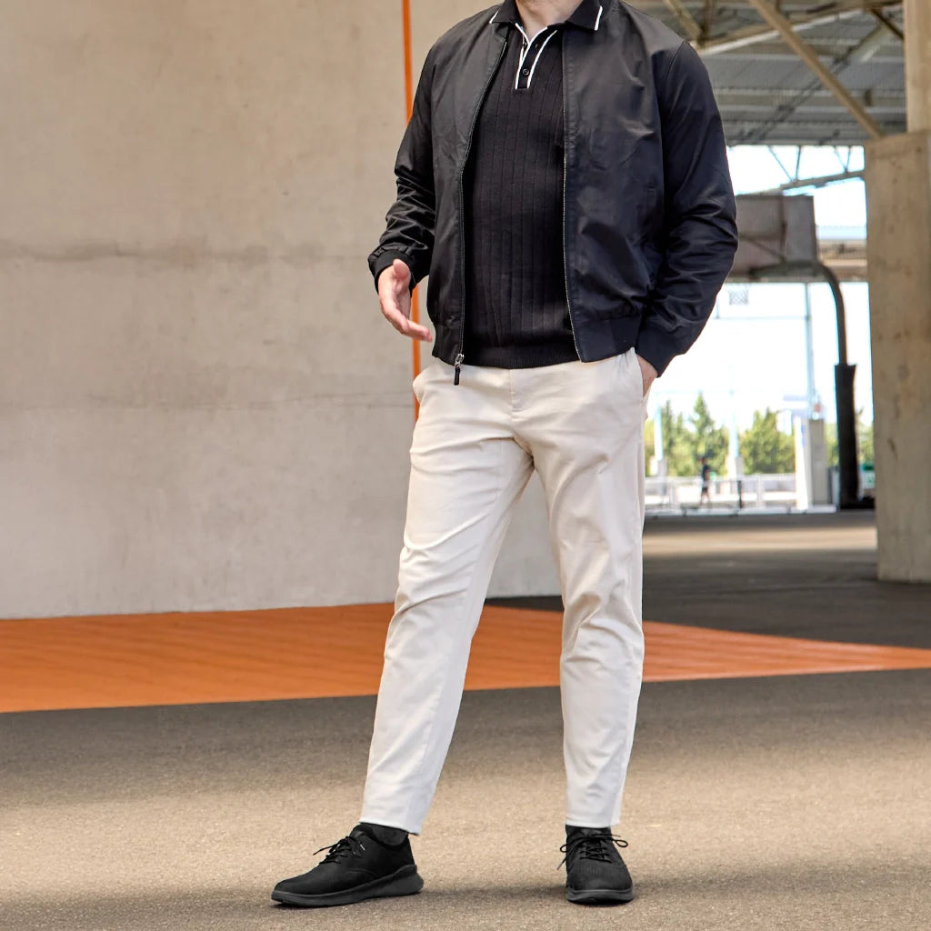 Person wearing a black jacket, black shirt, white pants, and black shoes standing outdoors.