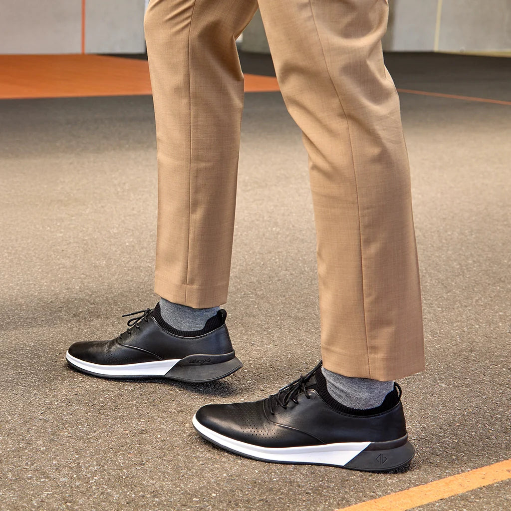 Person wearing black sneakers with white soles on a pavement background