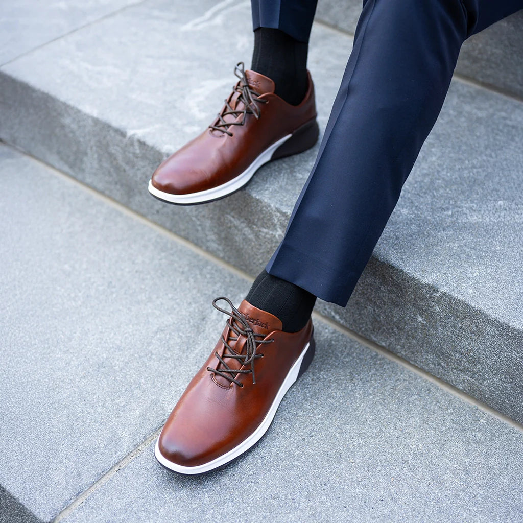 Brown leather shoes worn with a navy suit on a stone pavement.