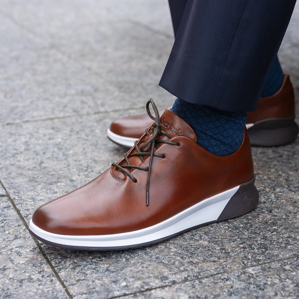 Brown leather shoes with white sole worn on a pavement