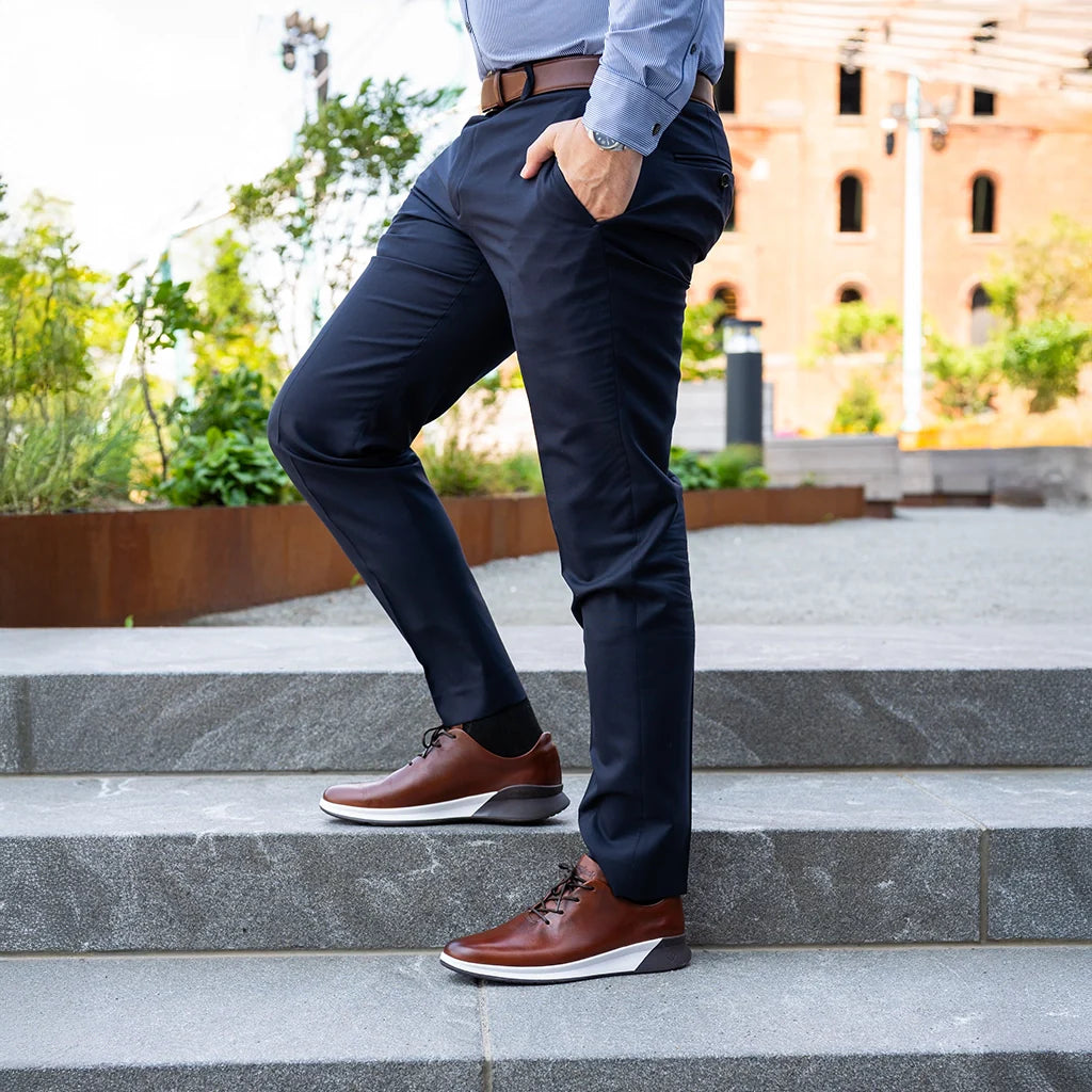 Person wearing navy pants and brown shoes standing on steps outdoors.
