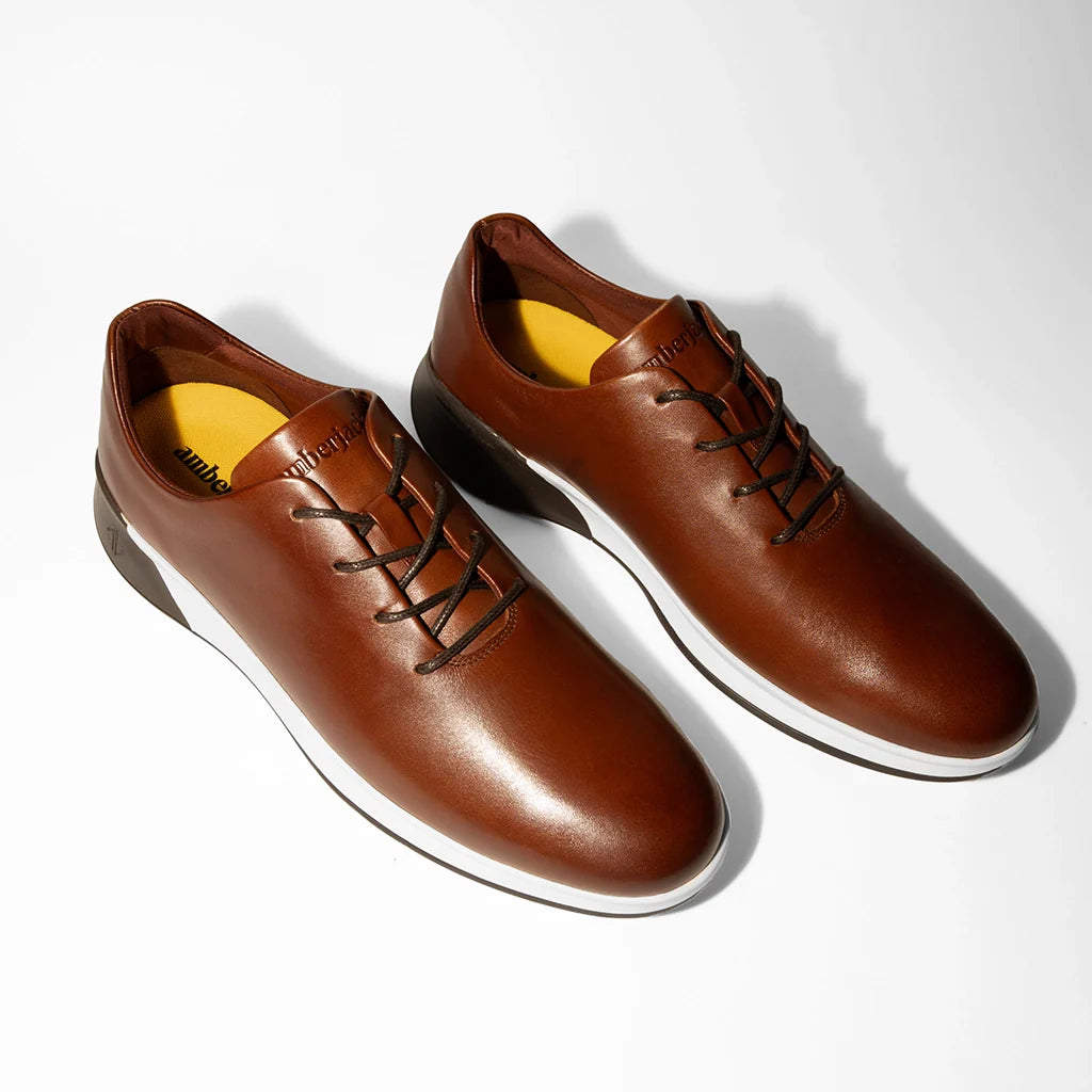 Pair of brown leather shoes with white soles on a light gray background