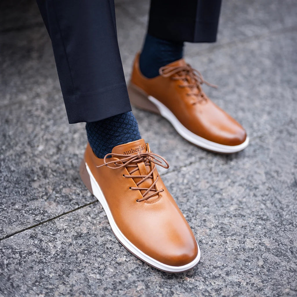 Brown leather shoes with white soles worn on a gray pavement