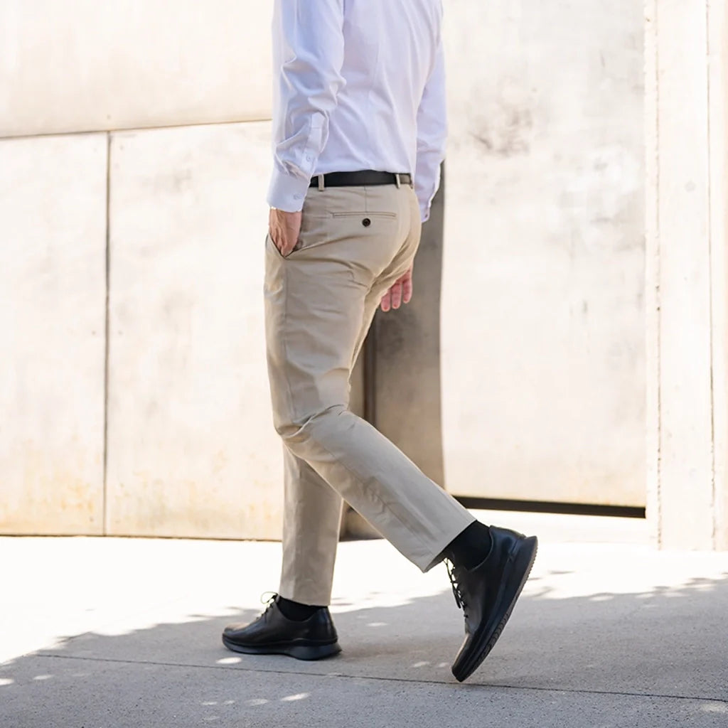 Person wearing beige pants and black shoes walking on a sidewalk.