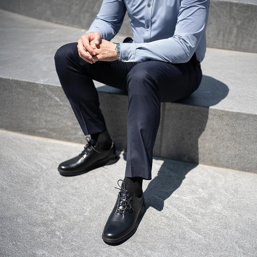 Person wearing a light blue shirt, dark pants, and black shoes sitting on concrete steps.