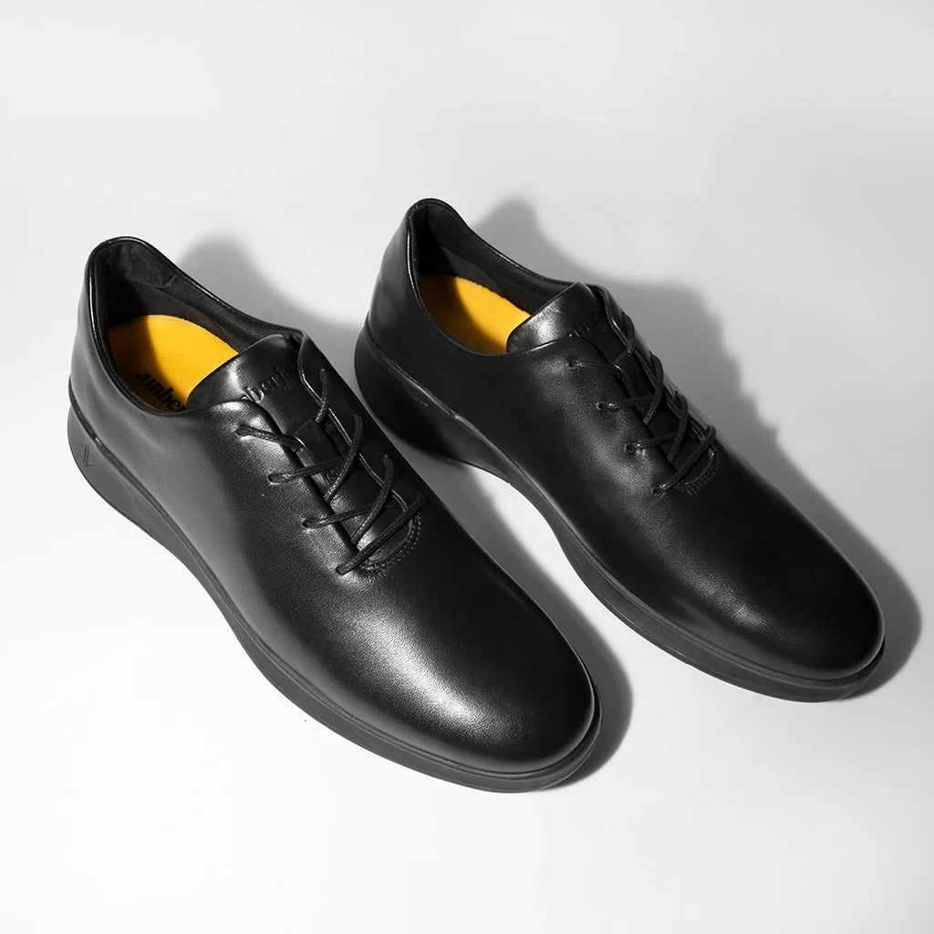 Pair of black leather shoes with yellow lining on a light gray background