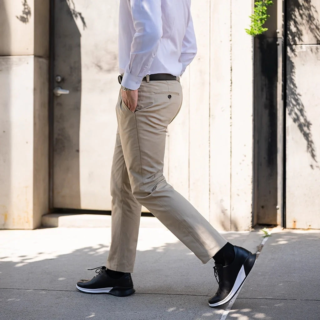 Person wearing beige pants and black shoes walking on a sidewalk.