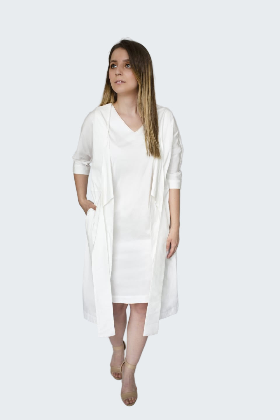 Woman wearing a white dress and cardigan against a plain background