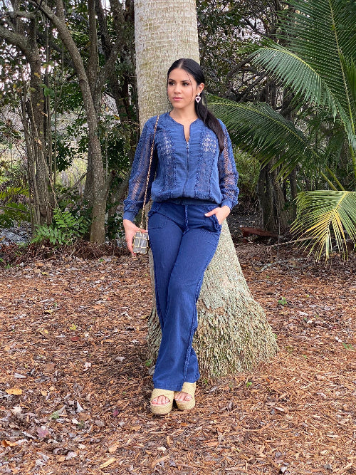 Woman in a blue outfit standing in a natural setting with trees and plants.
