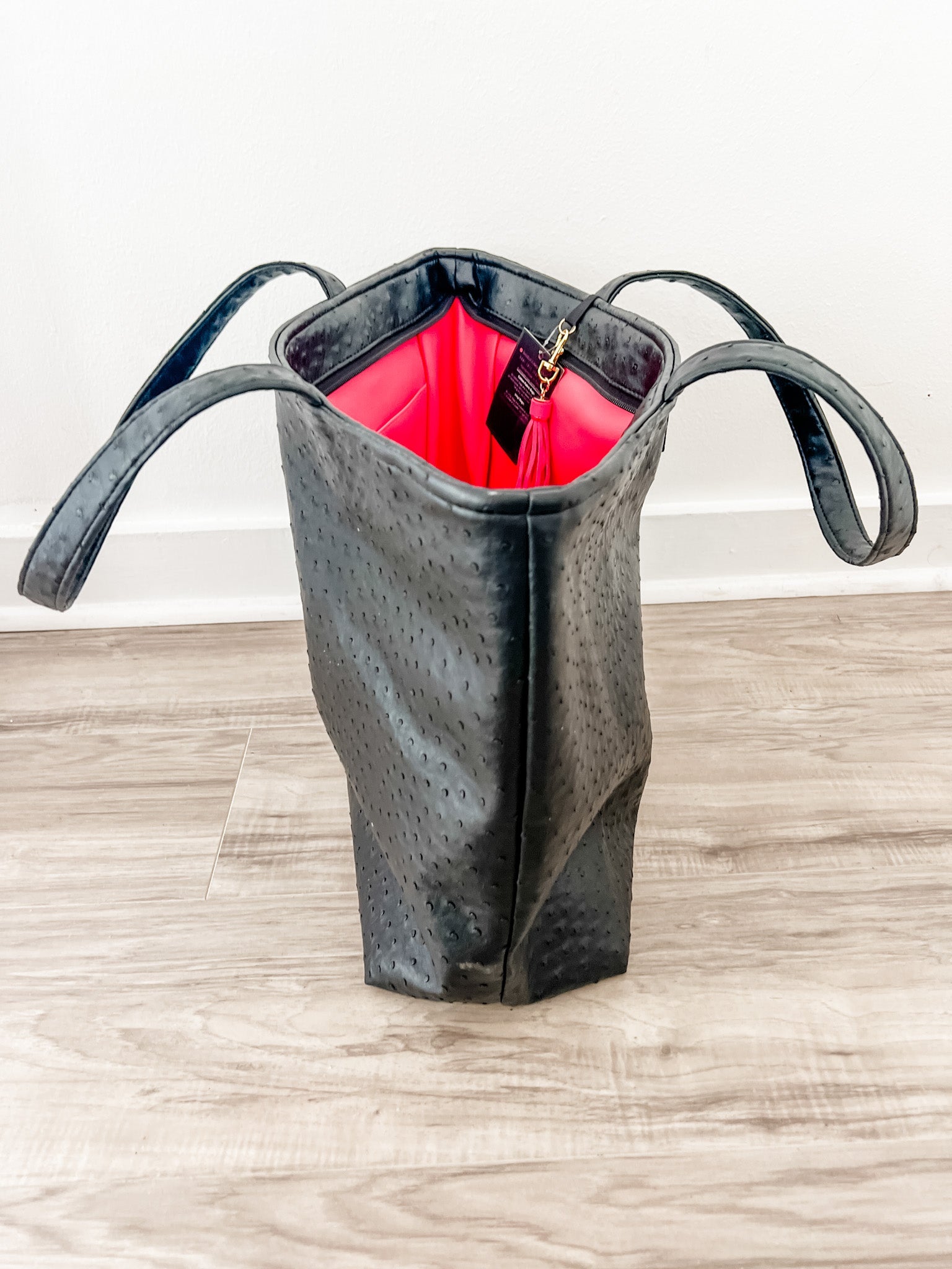Black textured handbag with red interior on a wooden surface