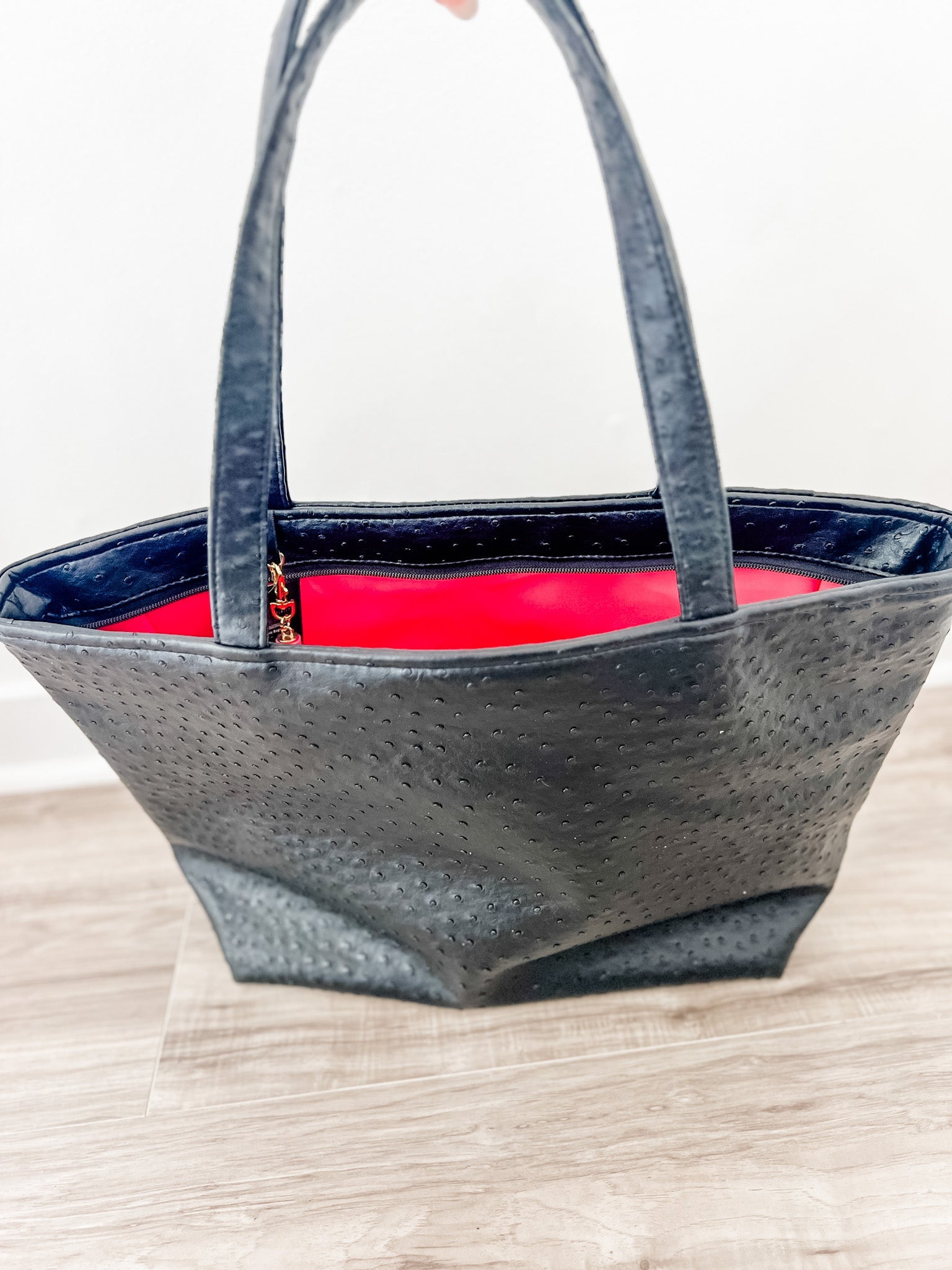 Black textured tote bag with red interior on a light wooden surface