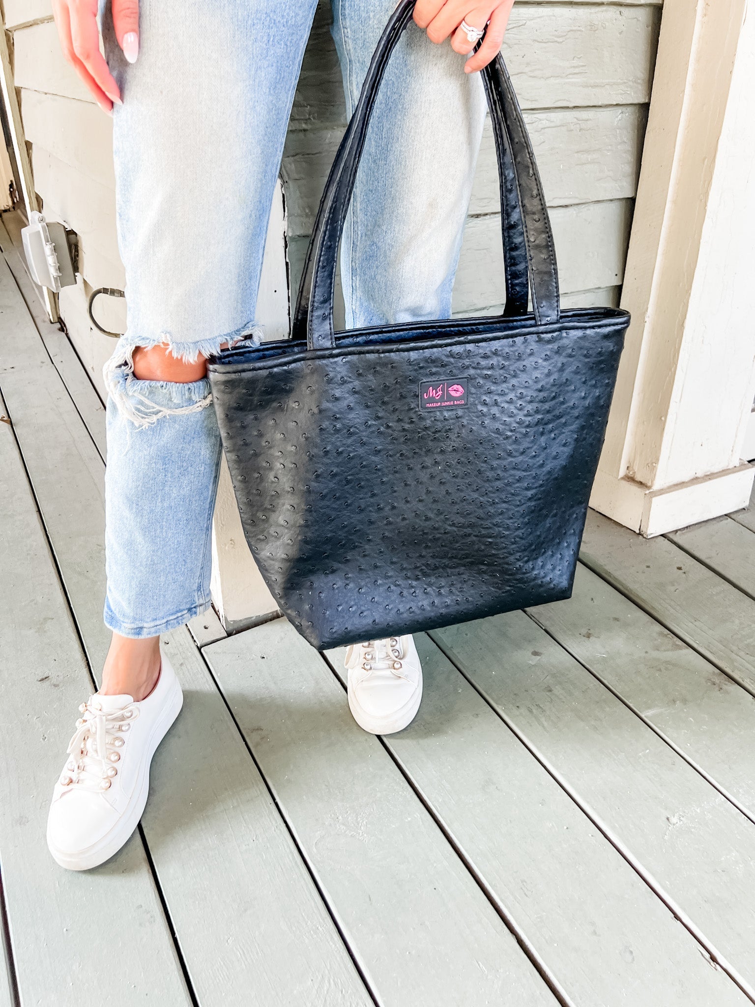 Person holding a black textured tote bag on a wooden deck
