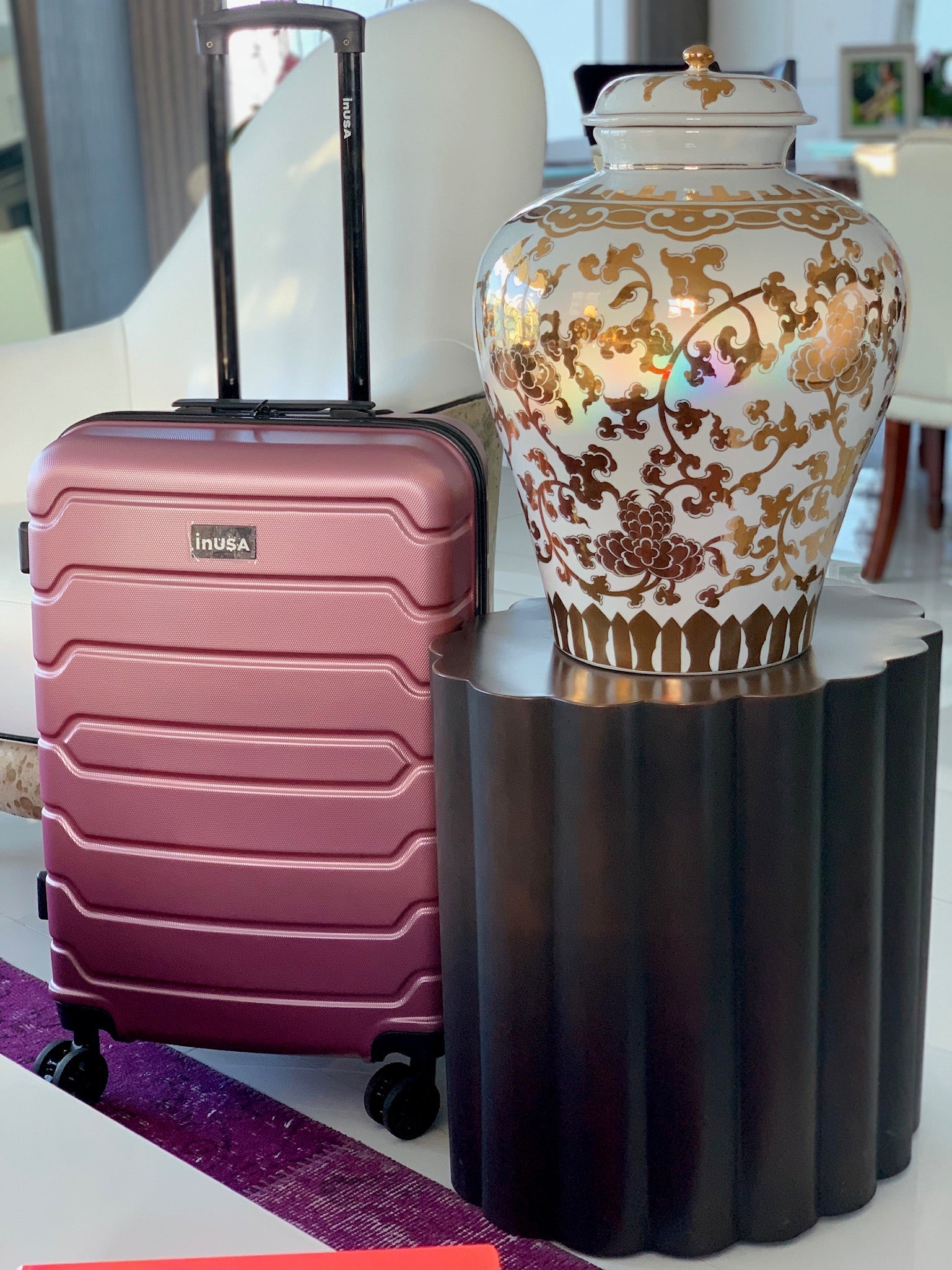 Pink suitcase next to a decorative vase on a table