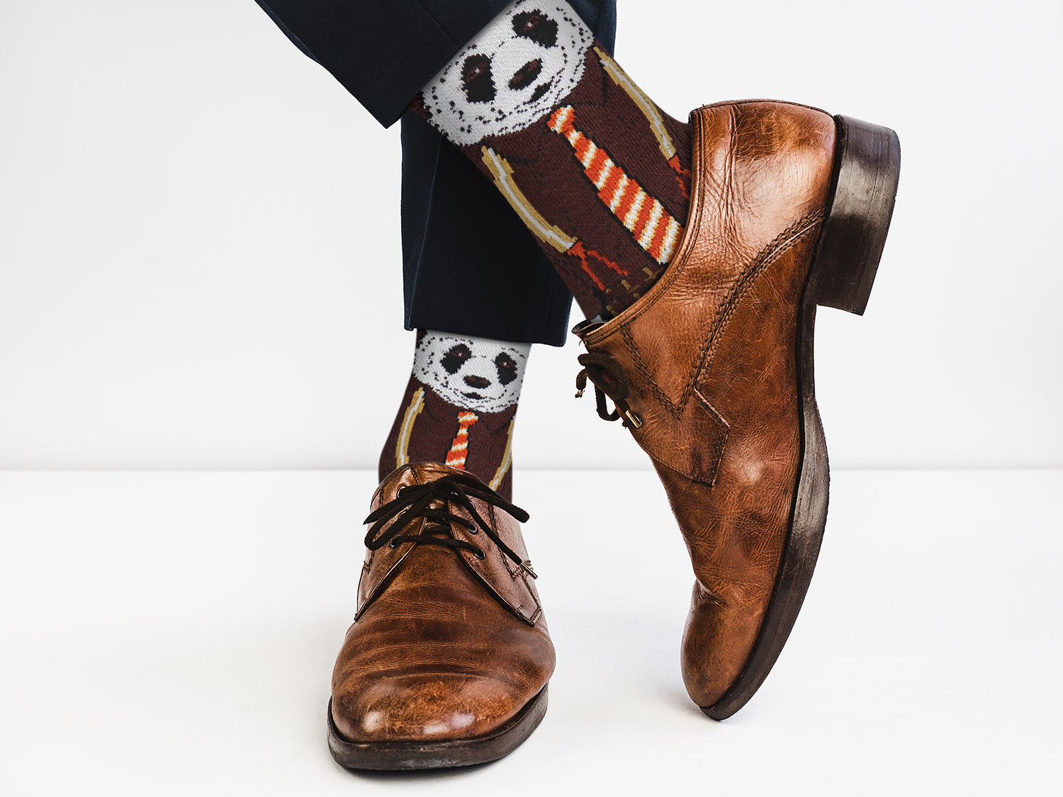 Brown dress shoes with panda-themed socks on a white background