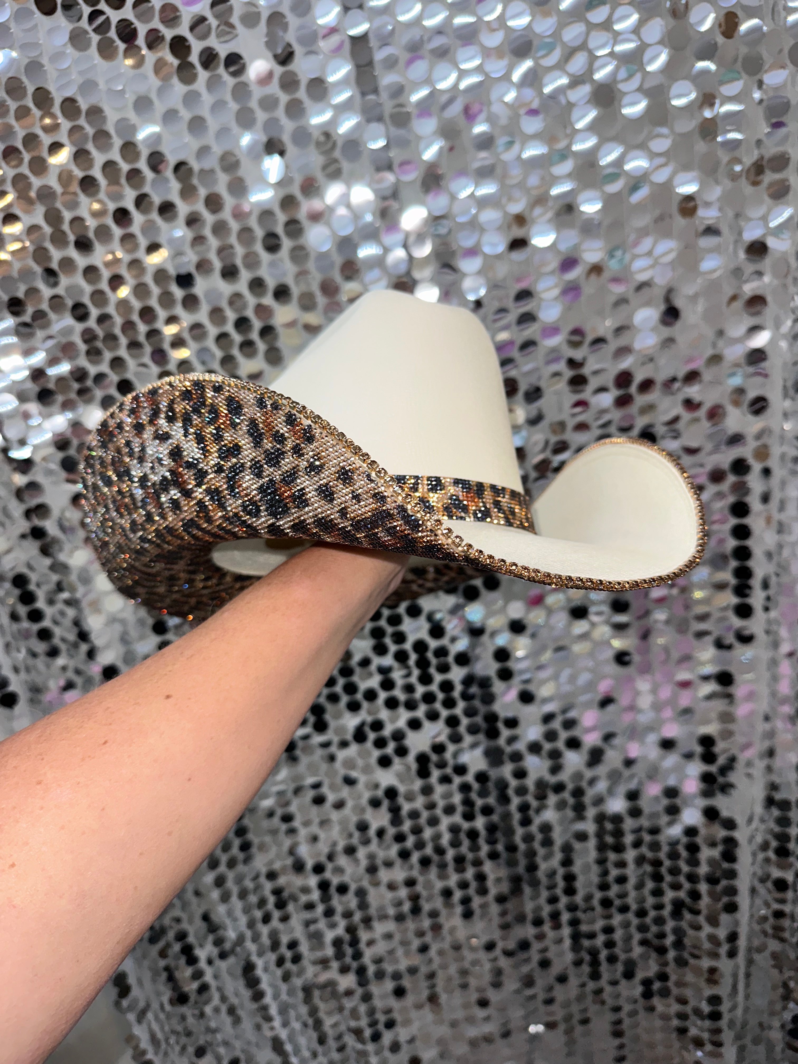 Cowboy hat held by a hand against a glittery silver background