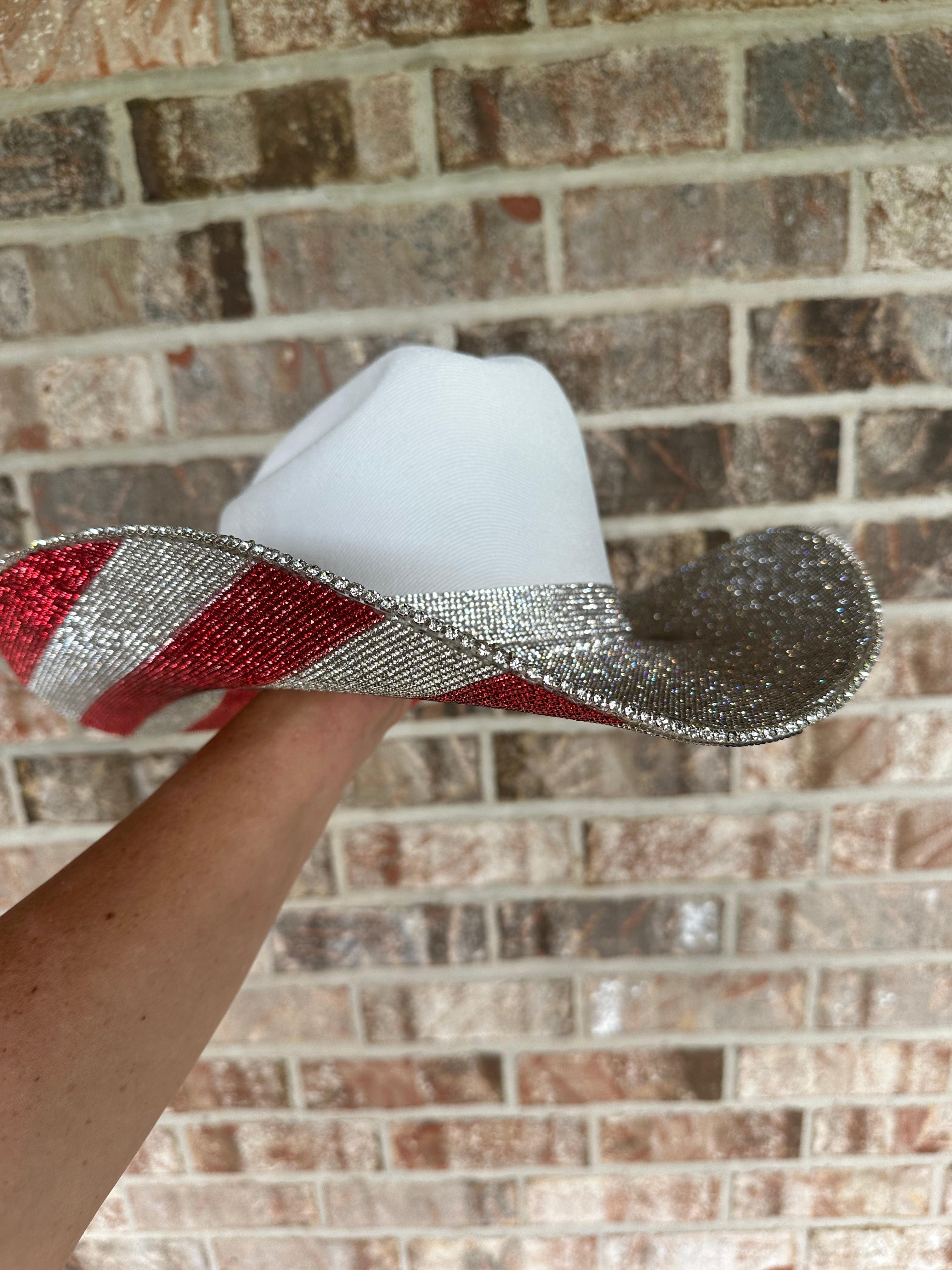 White cowboy hat with red and silver band held against a brick wall.