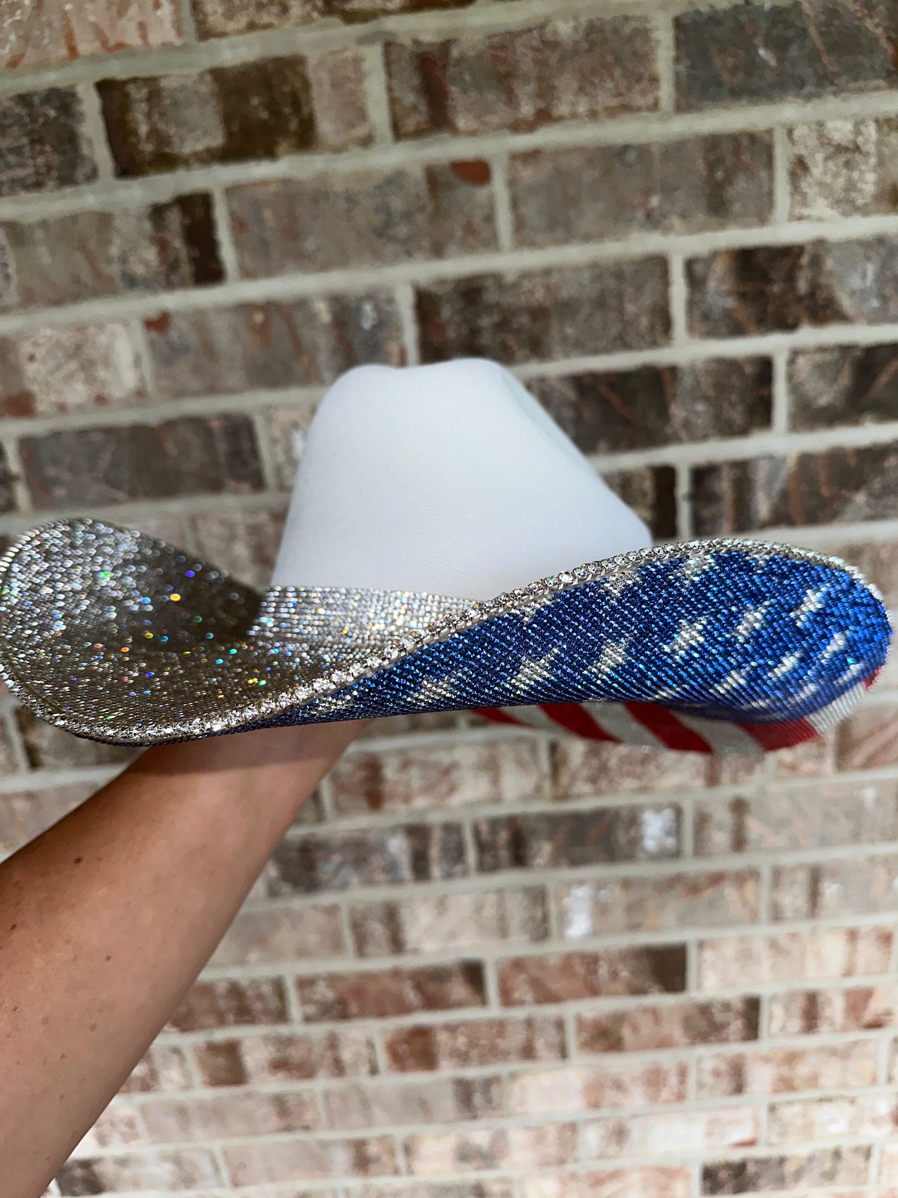 Shiny blue and silver slipper held against a brick wall.