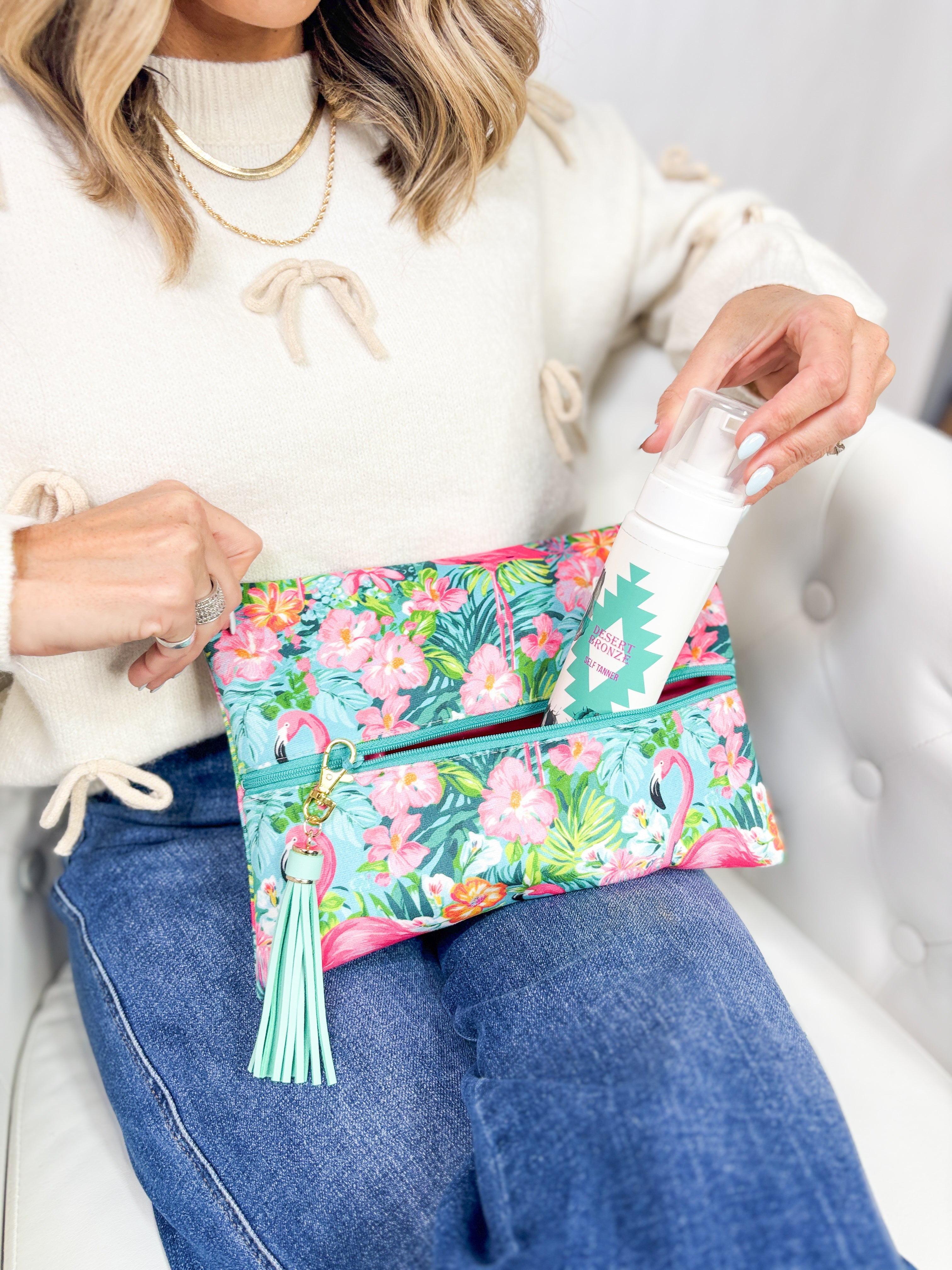 Person holding a floral clutch with a bottle, sitting on a white couch.