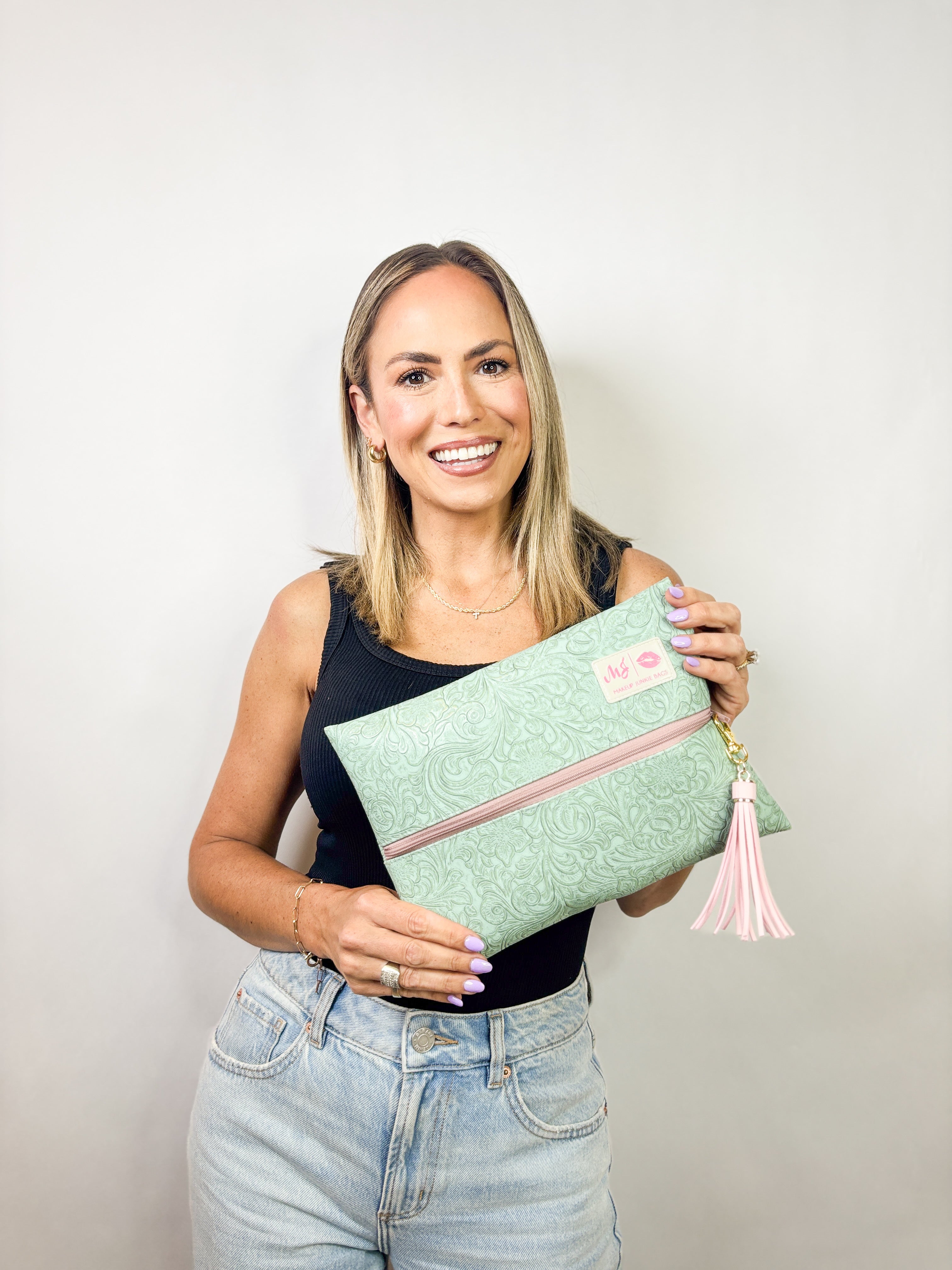 Woman holding a green clutch with a pink zipper and tassel against a plain background