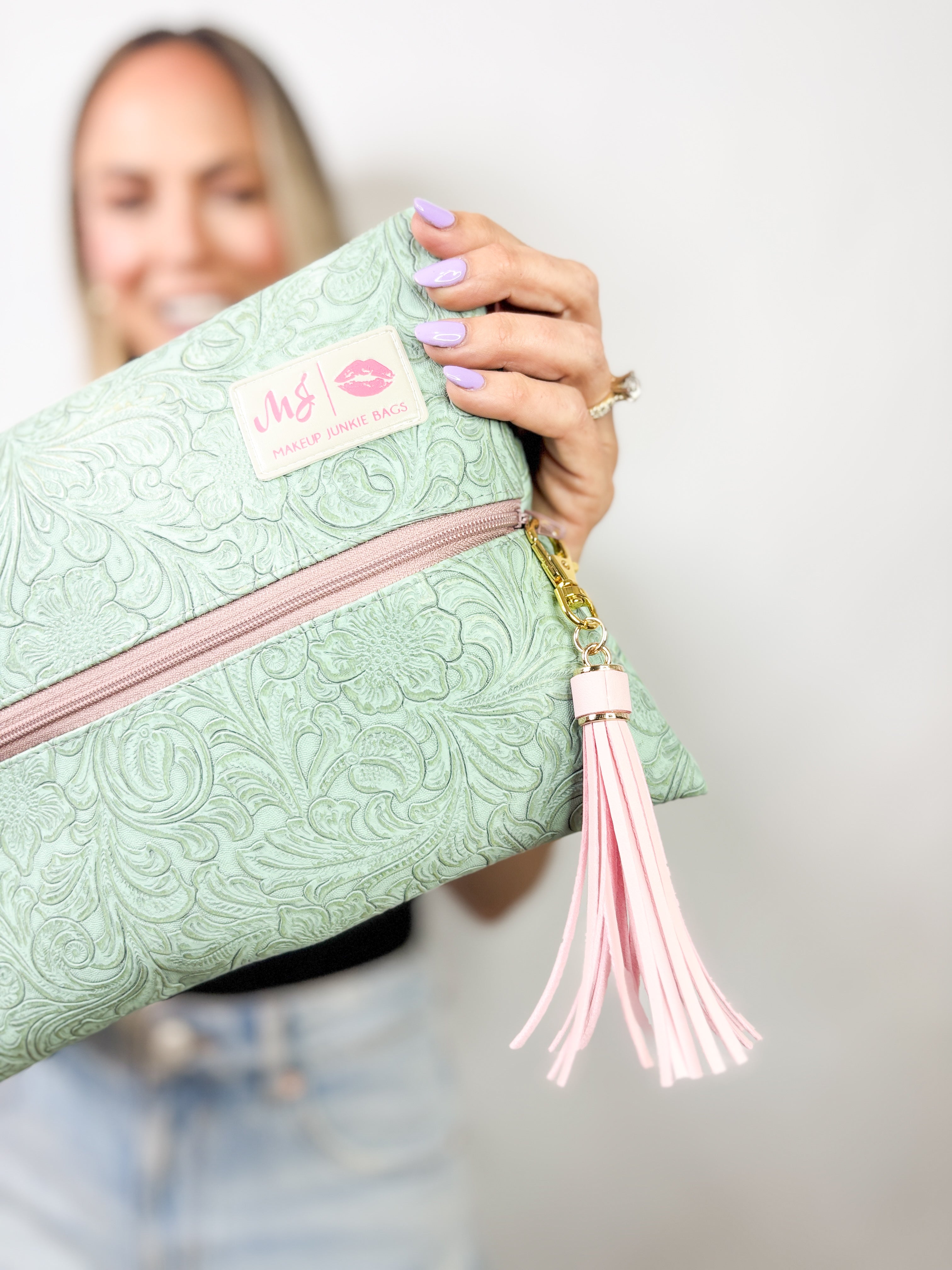 Mint green clutch bag with pink zipper and tassel held by a person against a white background