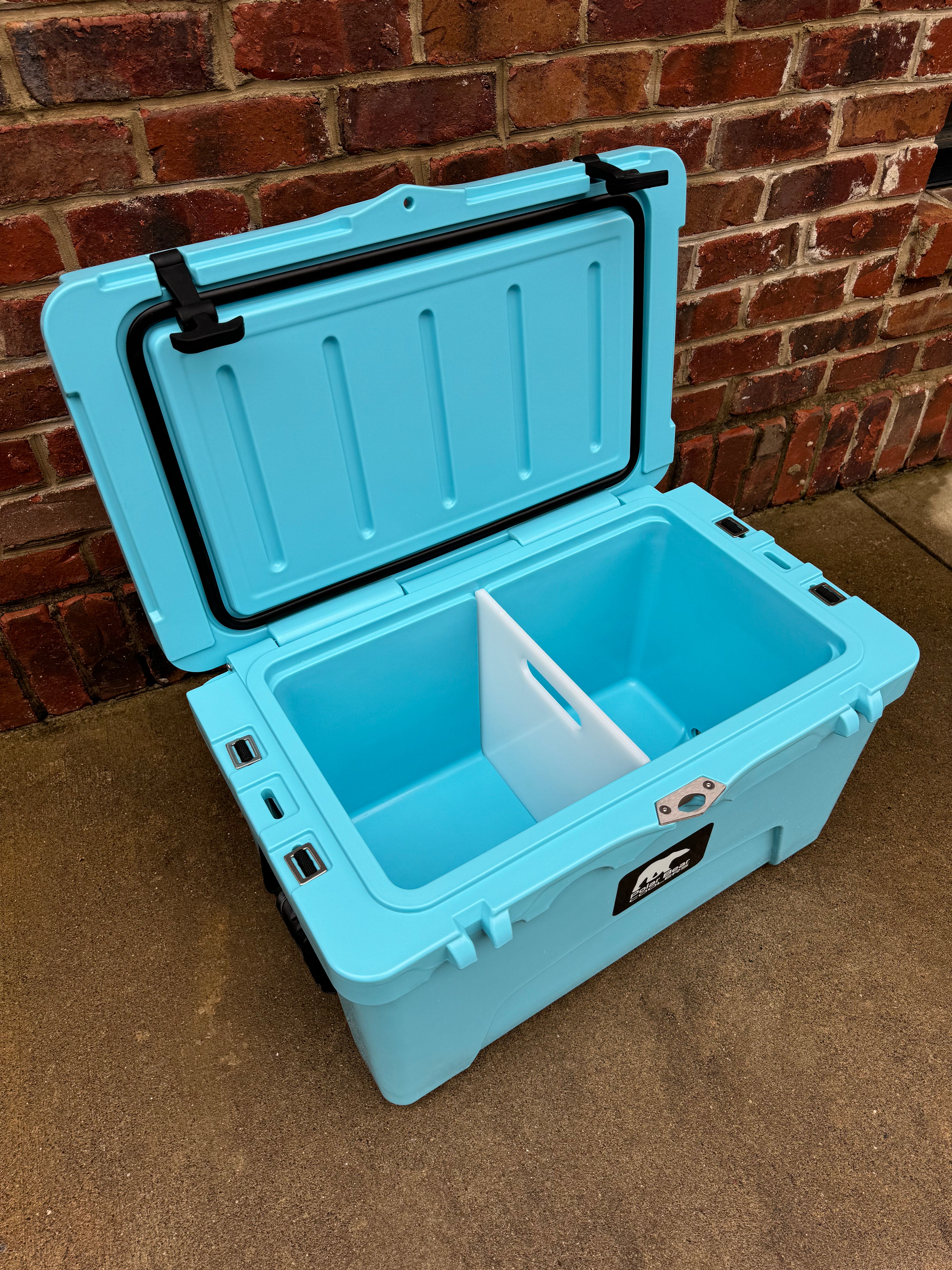 Blue cooler box with a black handle against a brick wall.