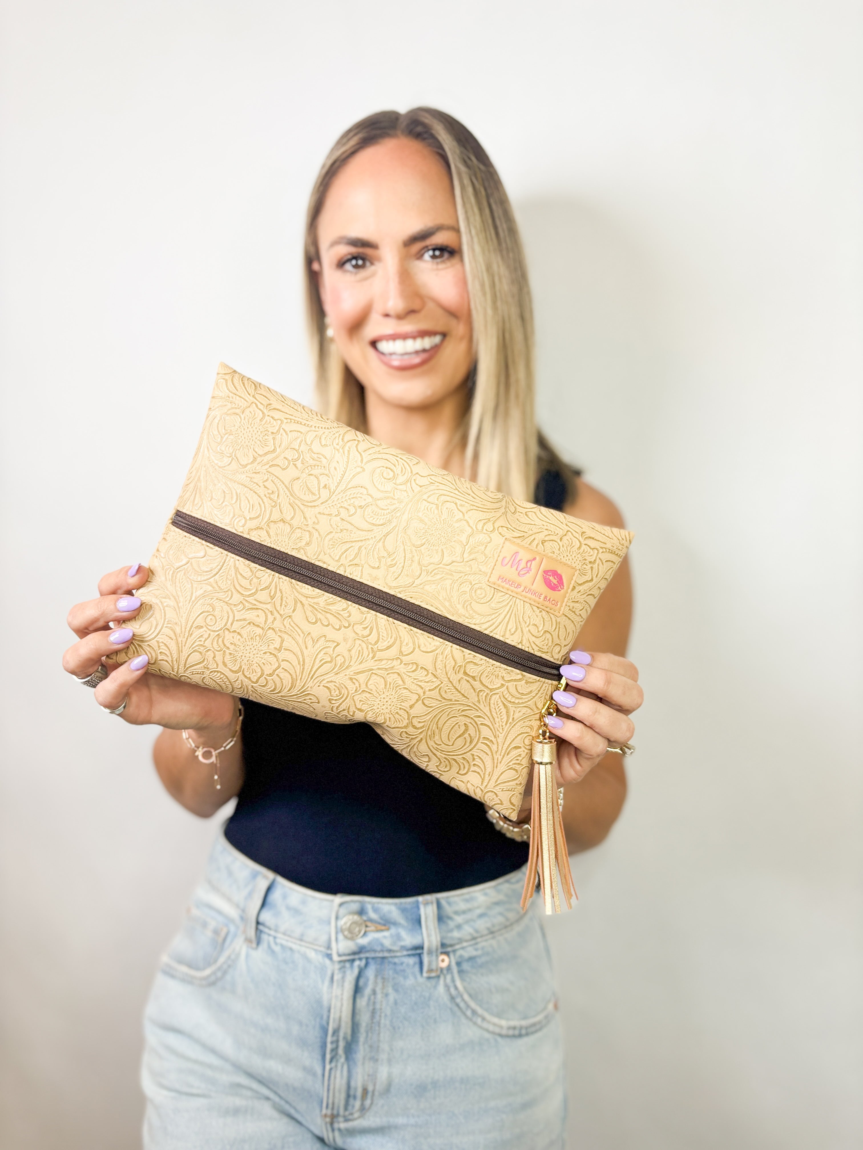 Woman holding a beige clutch bag with a visible brand logo against a plain background