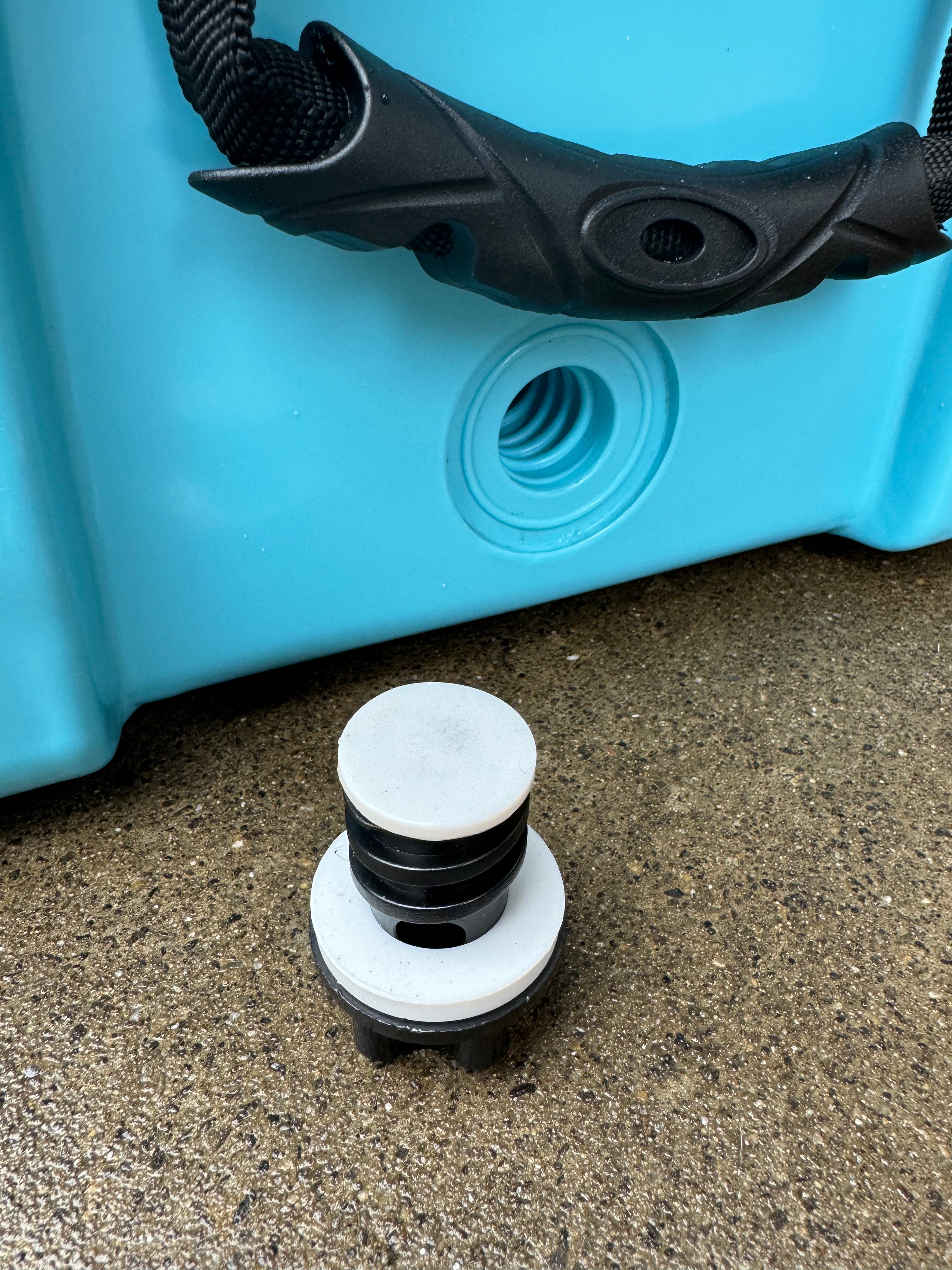 Close-up of a blue container with a black handle and a white and black valve on a concrete surface.