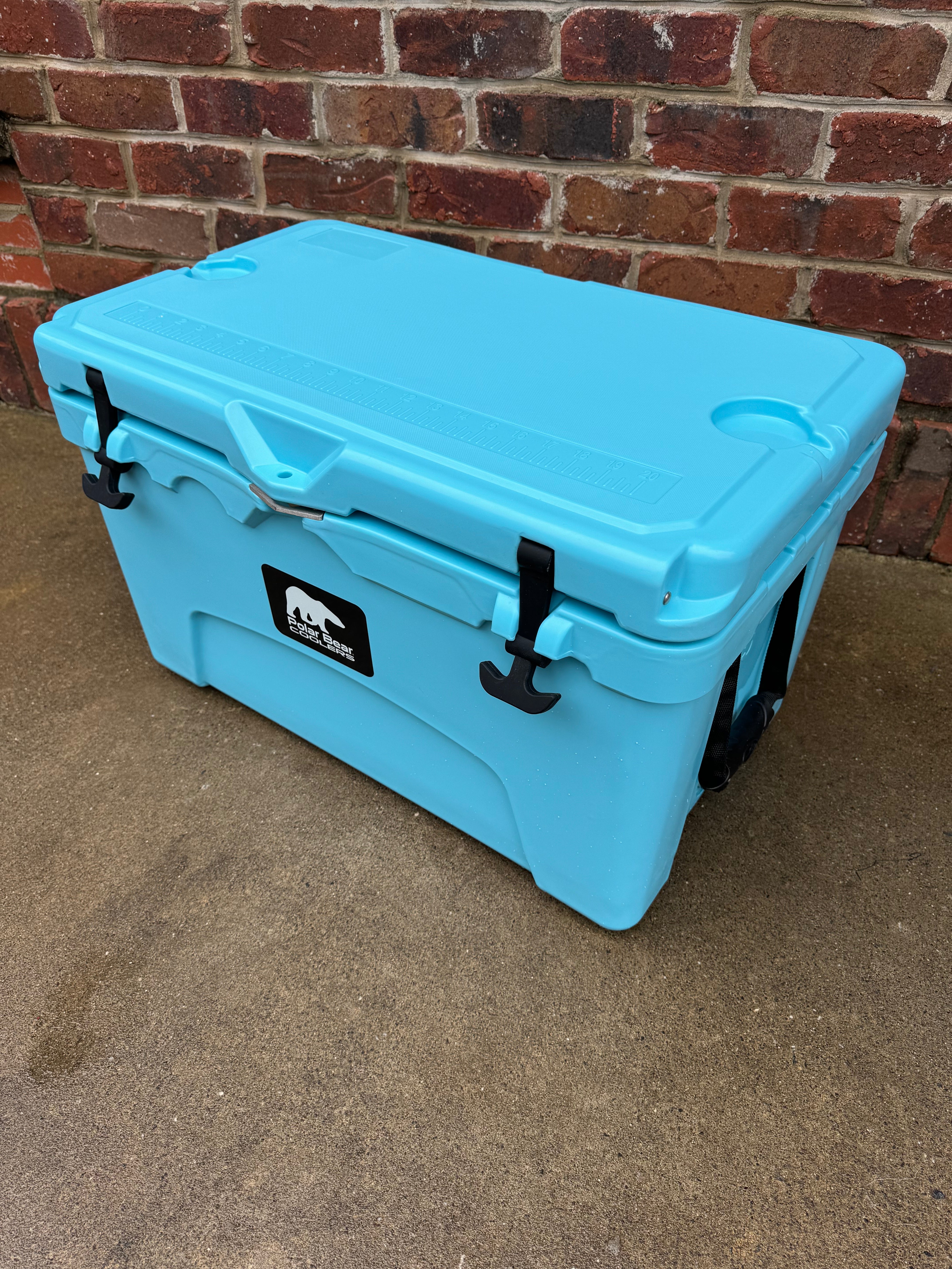 Blue cooler box with a brand logo on a concrete surface against a brick wall.