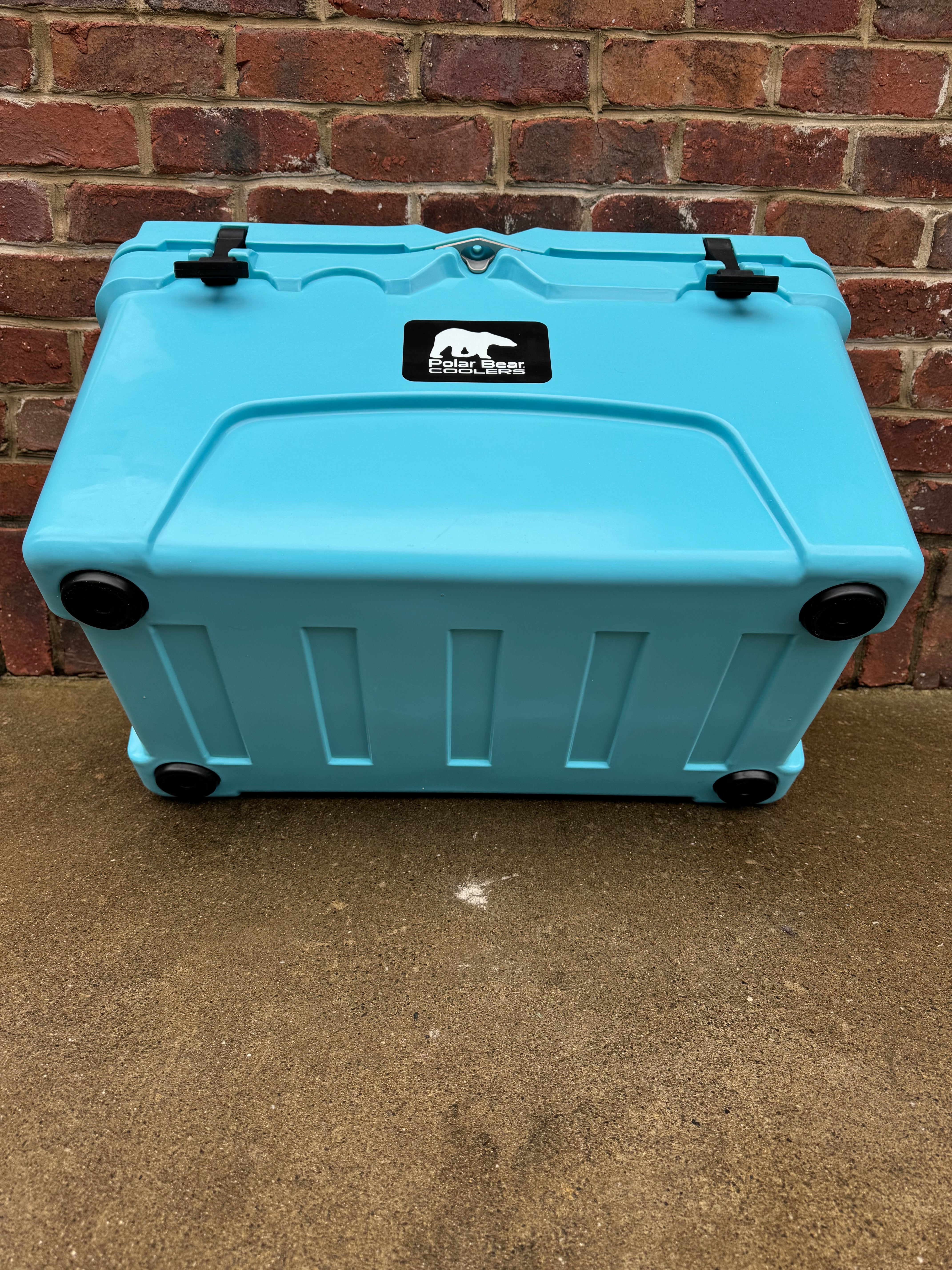 Blue cooler box with a logo on a concrete floor against a brick wall