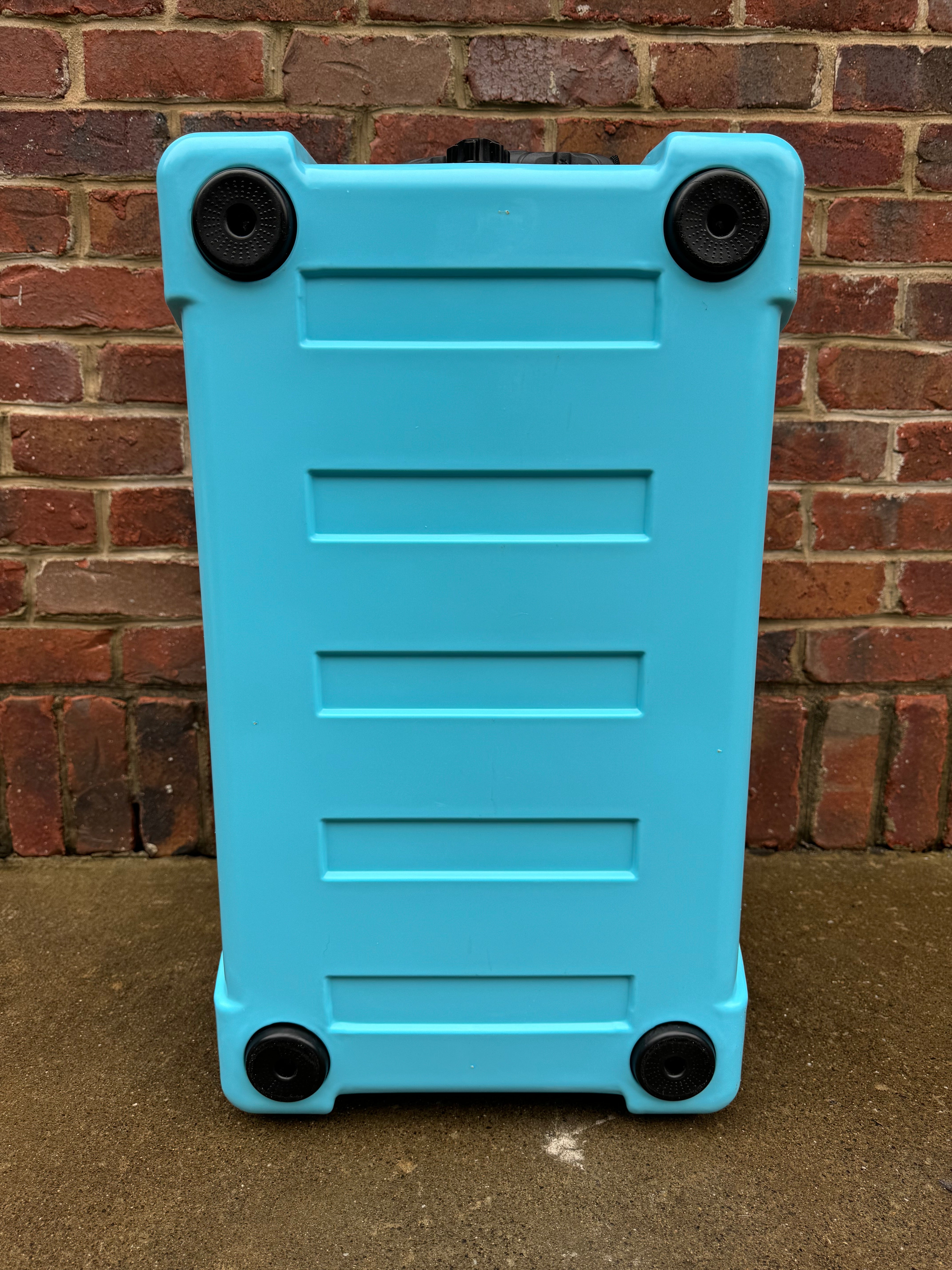 Blue suitcase with black wheels against a brick wall.