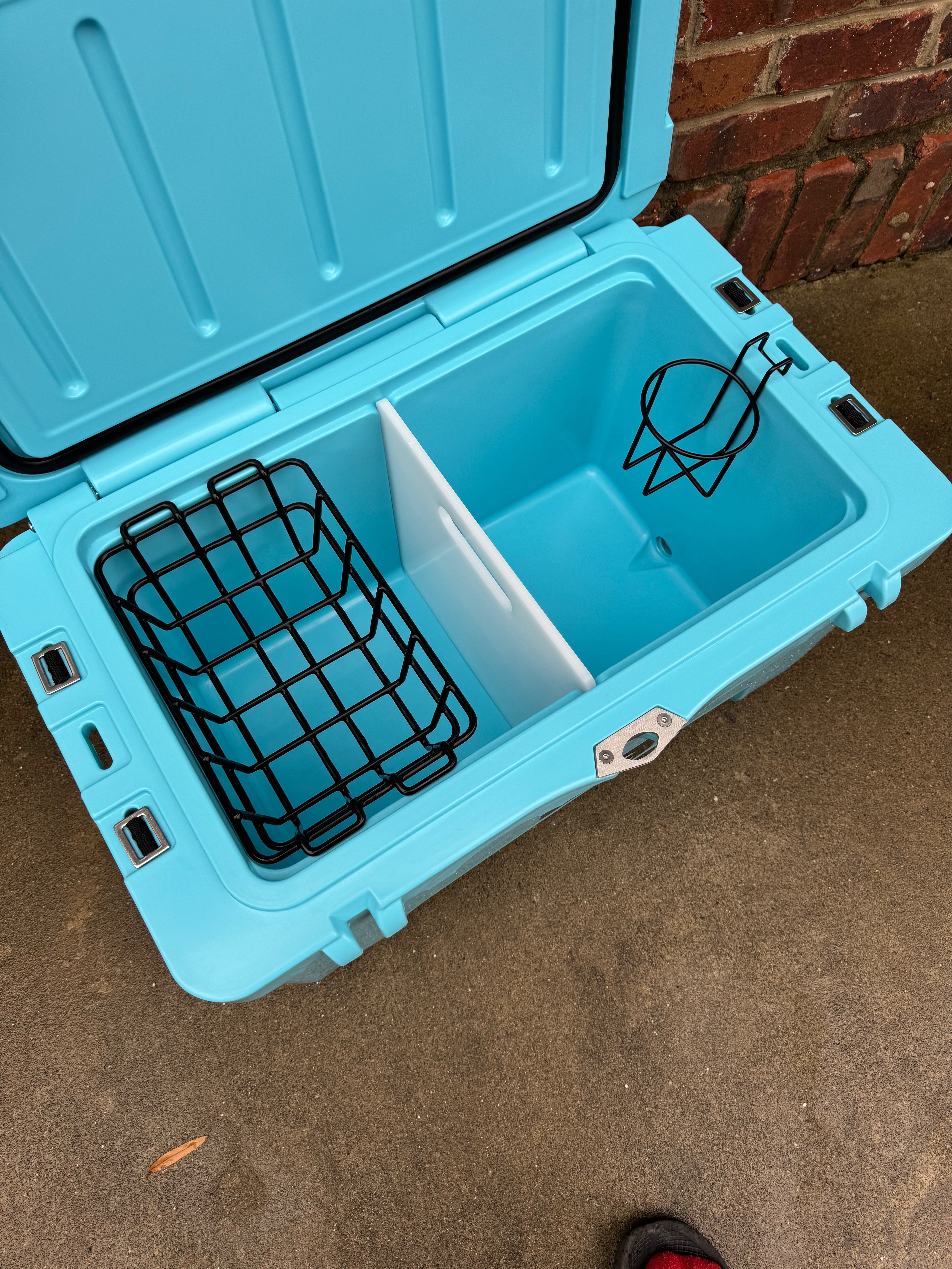 Blue cooler with a black wire basket on a concrete floor.