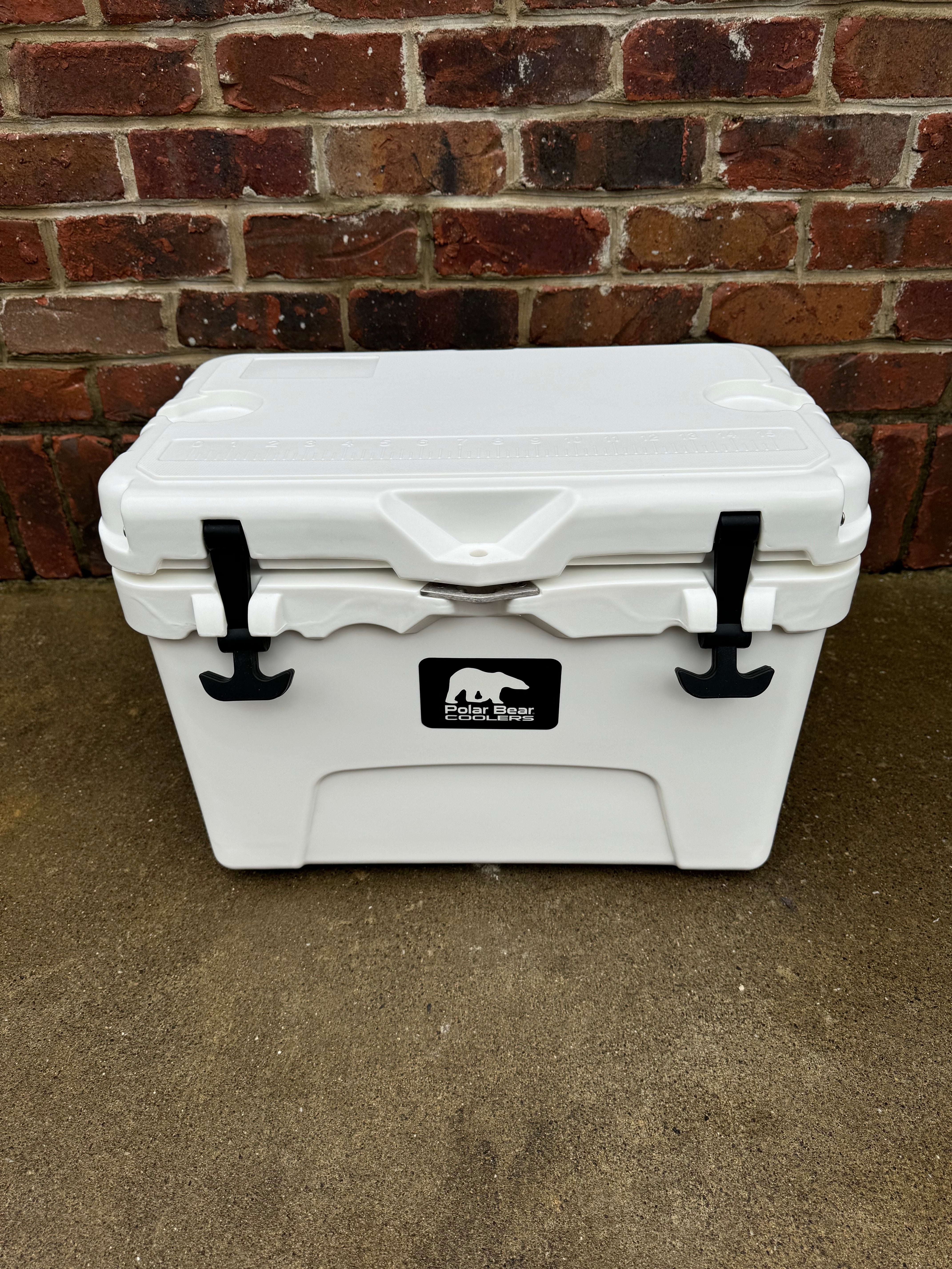 White cooler box with a logo on a concrete floor against a brick wall