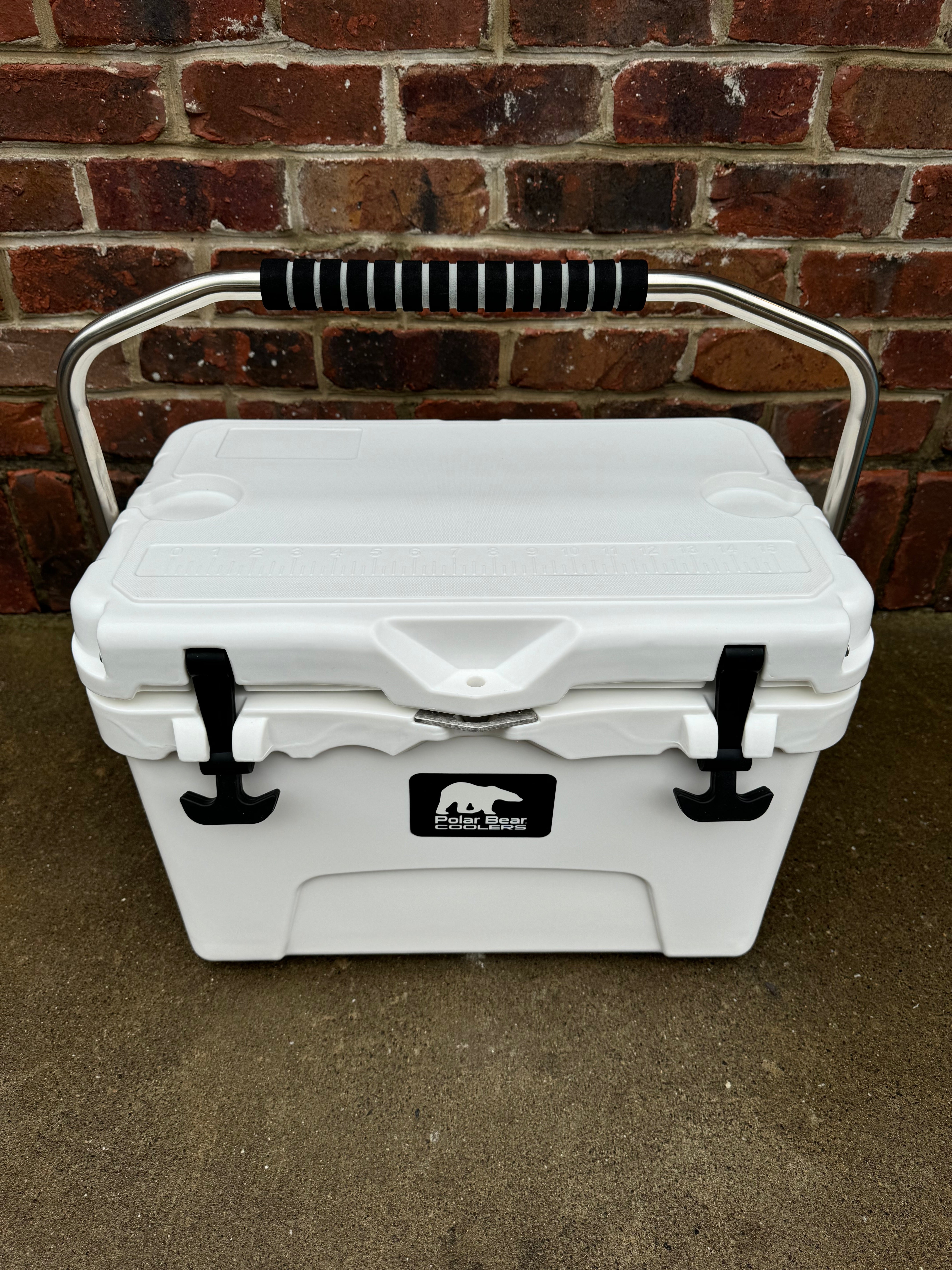 White cooler box with black handles and a logo on a brick wall background