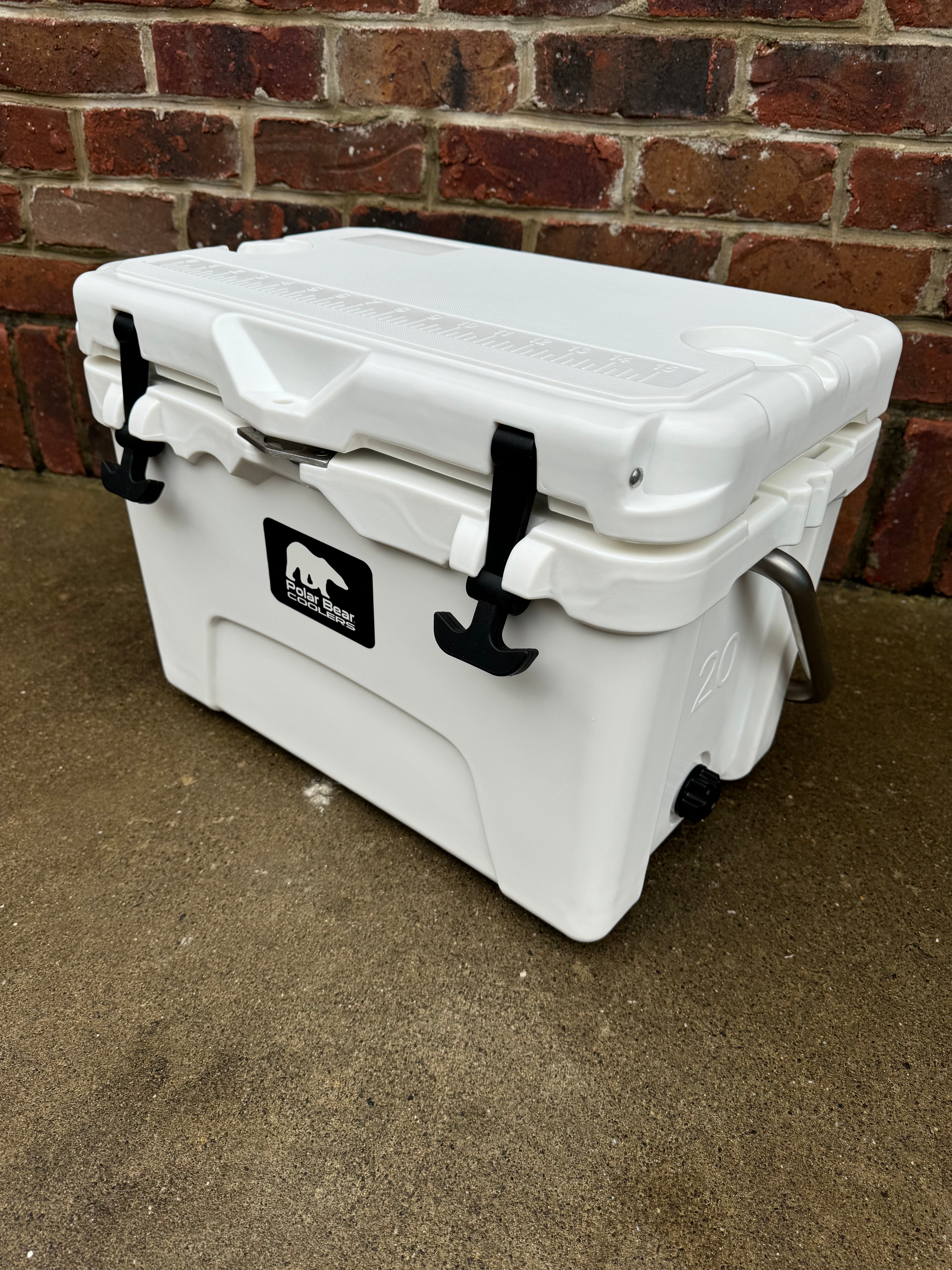 White cooler with a logo on a concrete floor against a brick wall