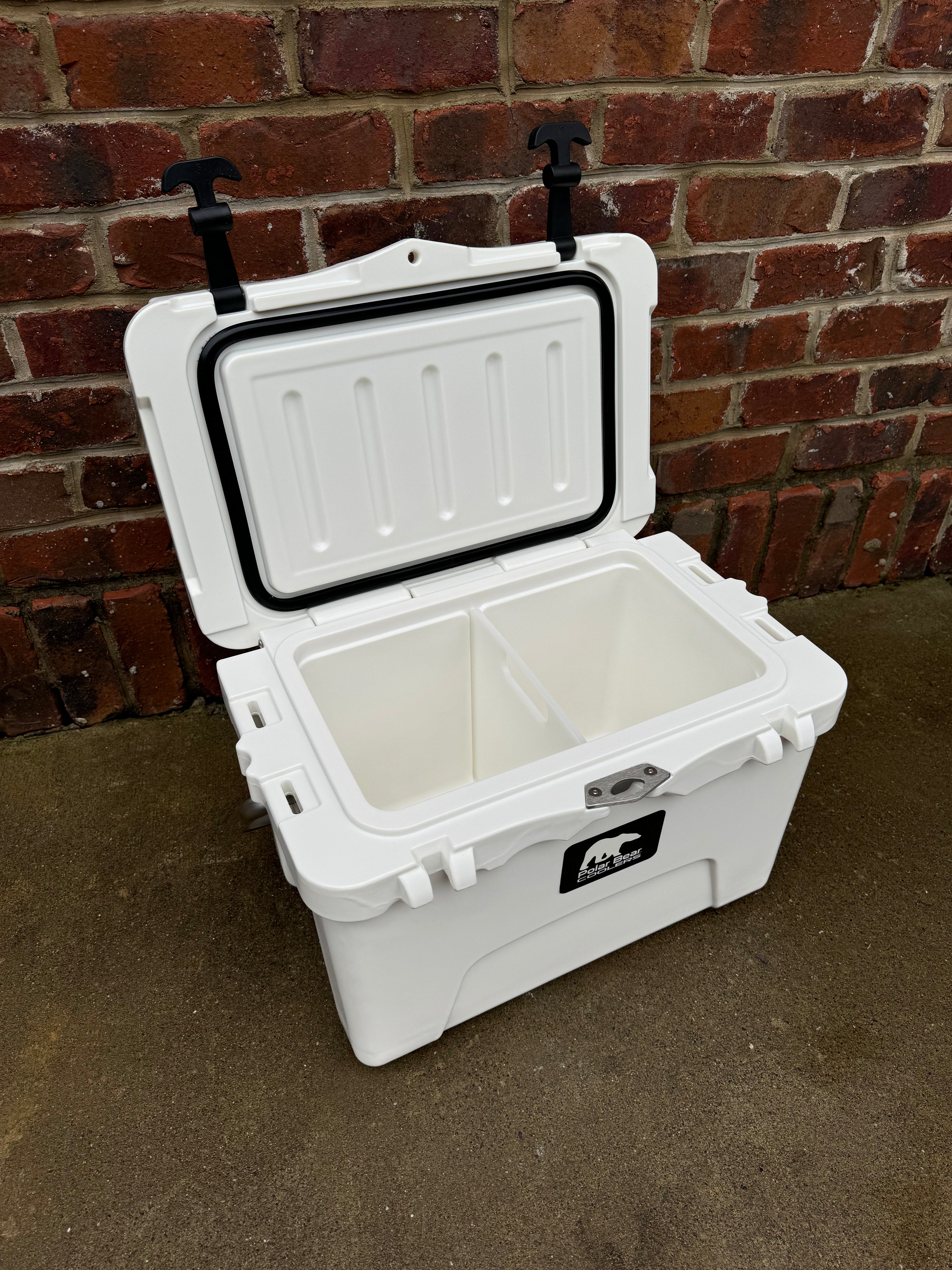 White cooler box with open lid against a brick wall.