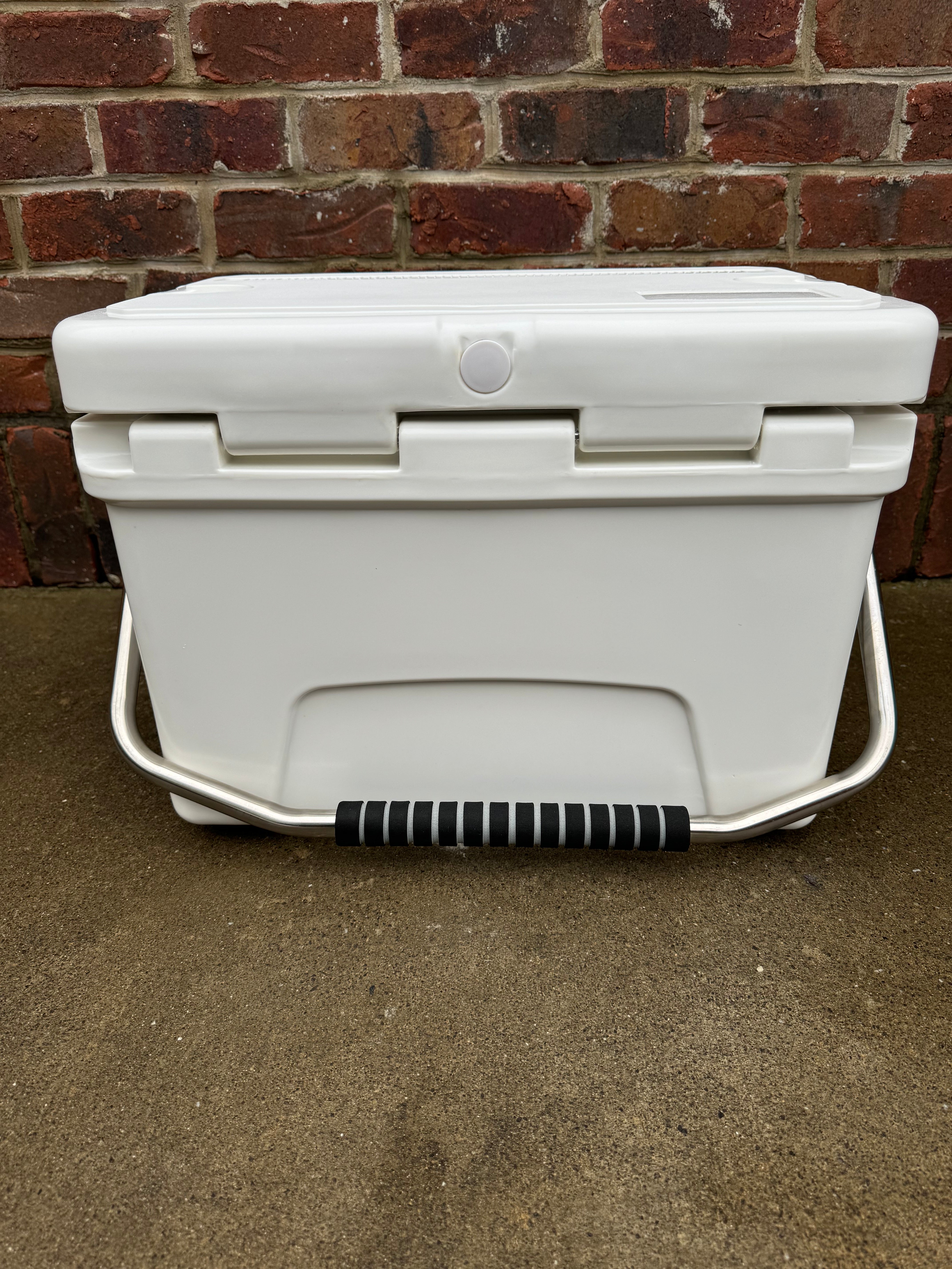 White cooler with a black handle against a brick wall.