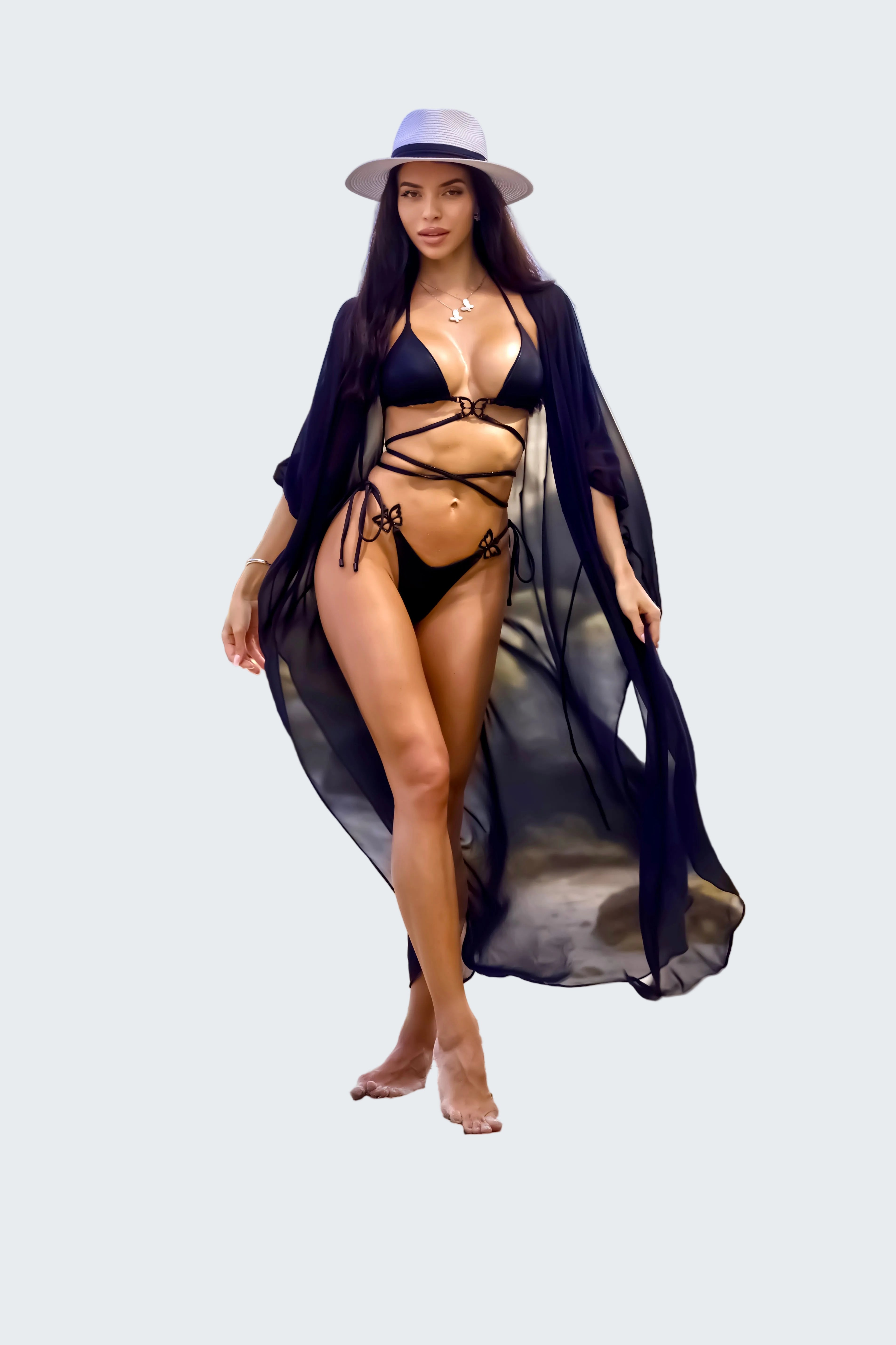 Woman in a black bikini and blue cover-up standing on a rocky beach with ocean in the background