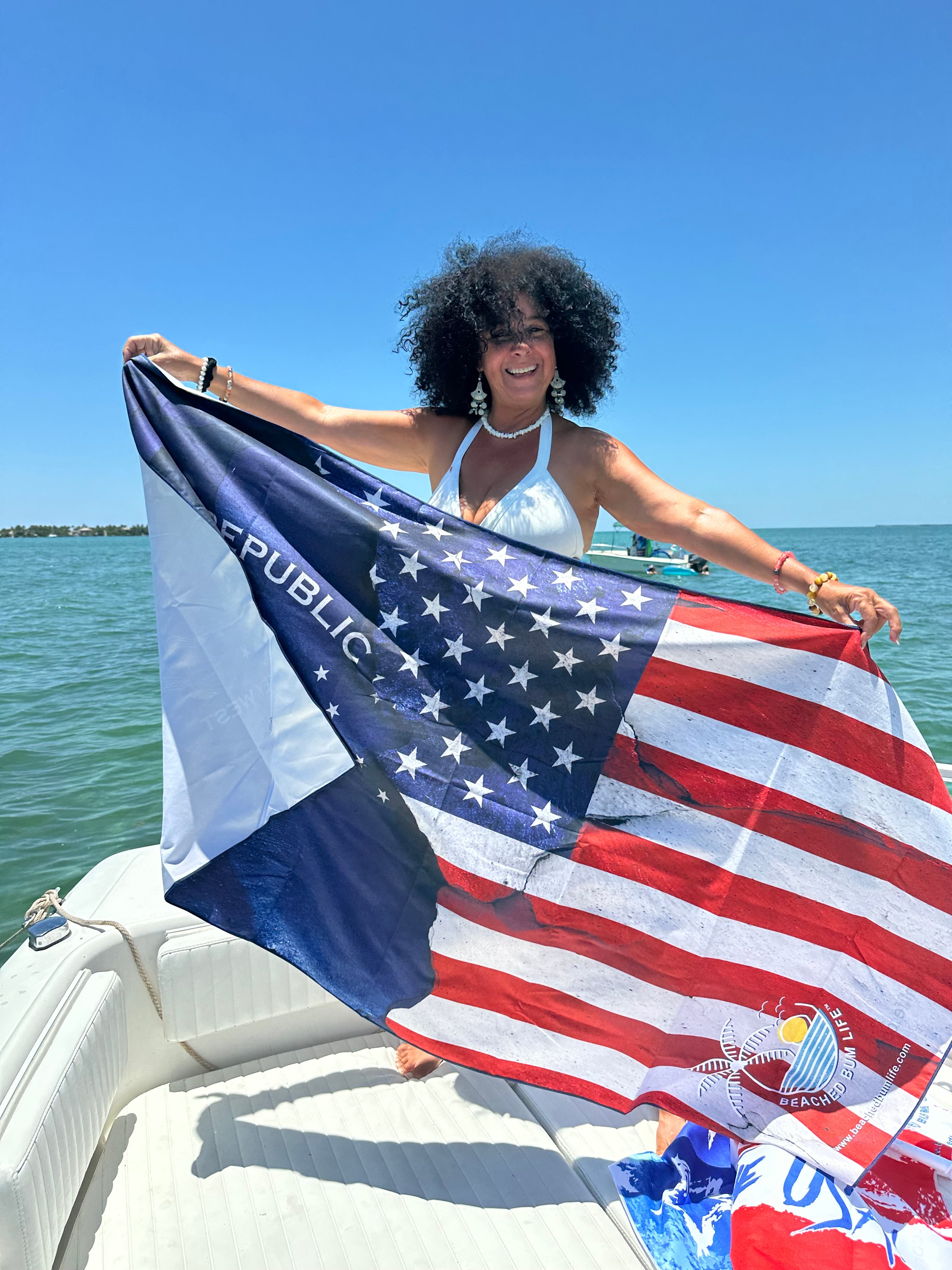 Person holding a large American flag on a boat with a clear blue sky and water background