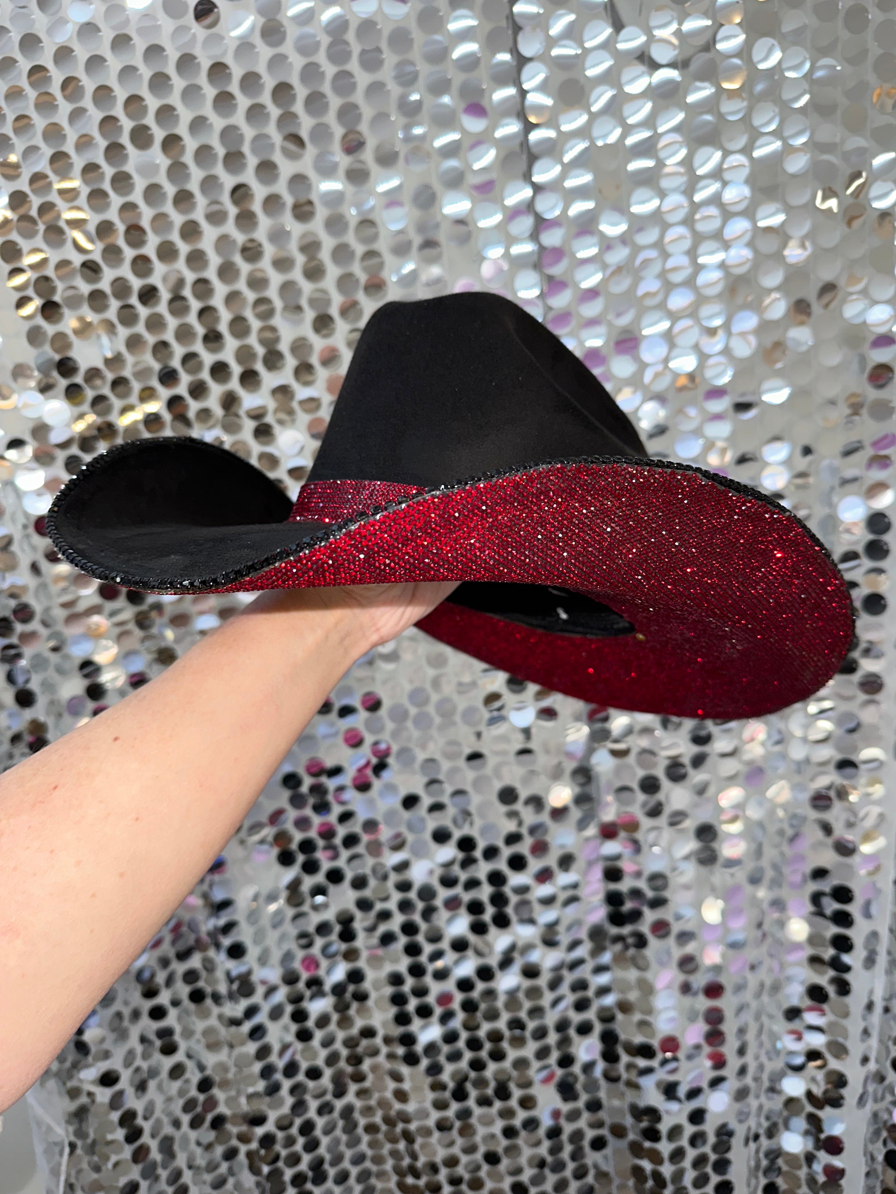 Black and red glittery bow held by a hand against a silver sequin background