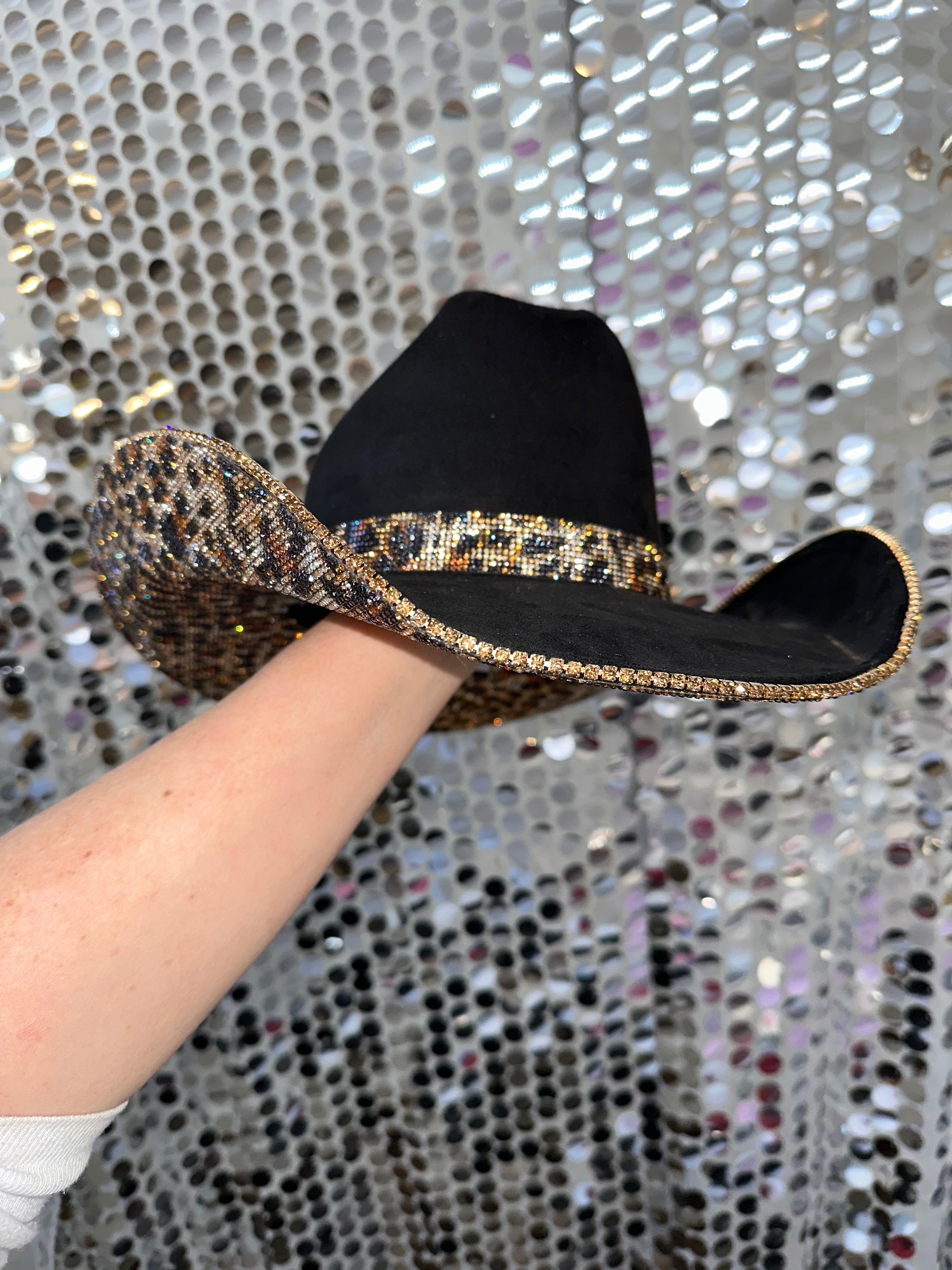 Black sandal with a decorative strap held by a hand against a glittery background